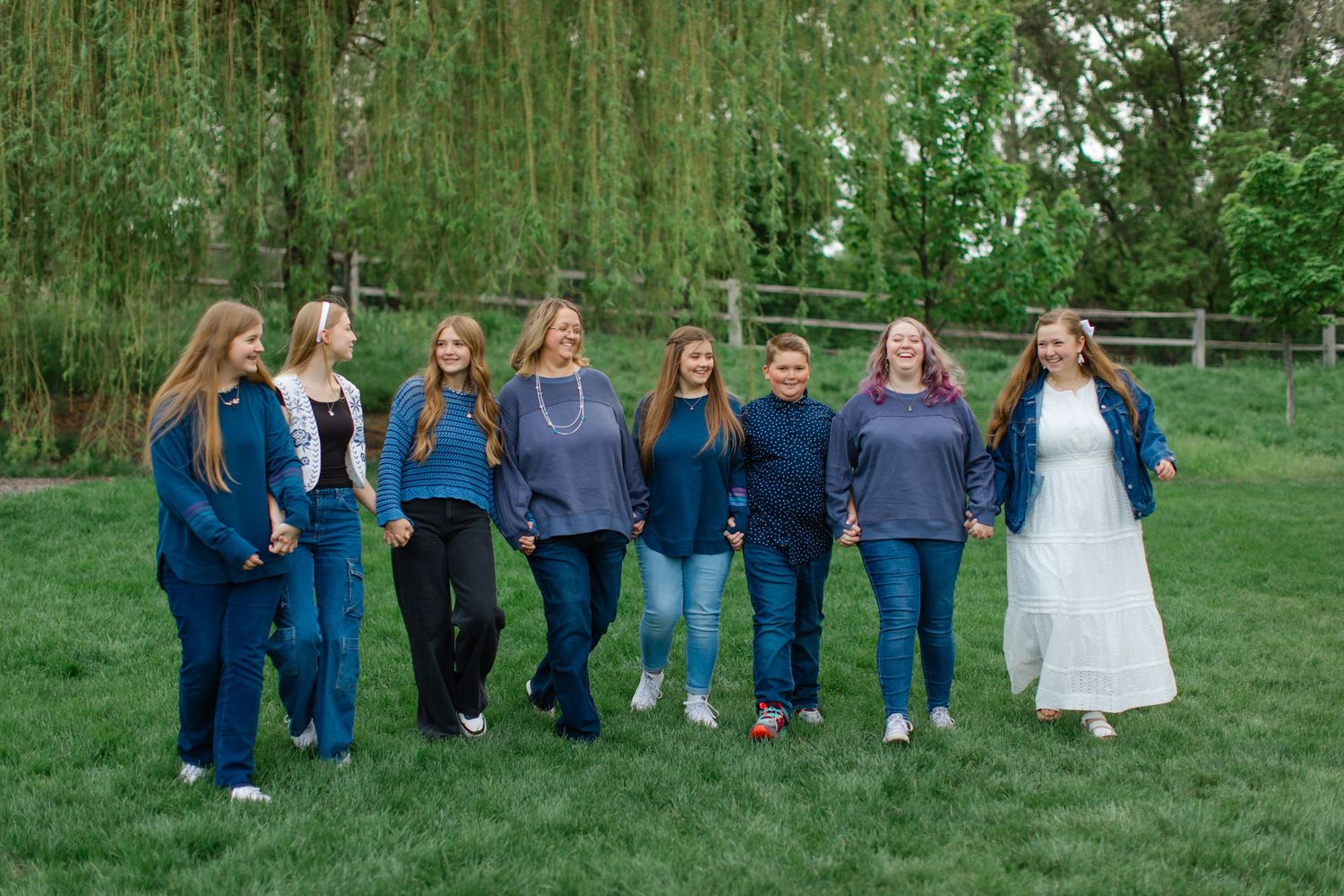 A group of people wearing blue jeans and casual attire stand together in a grassy outdoor setting for a photo.