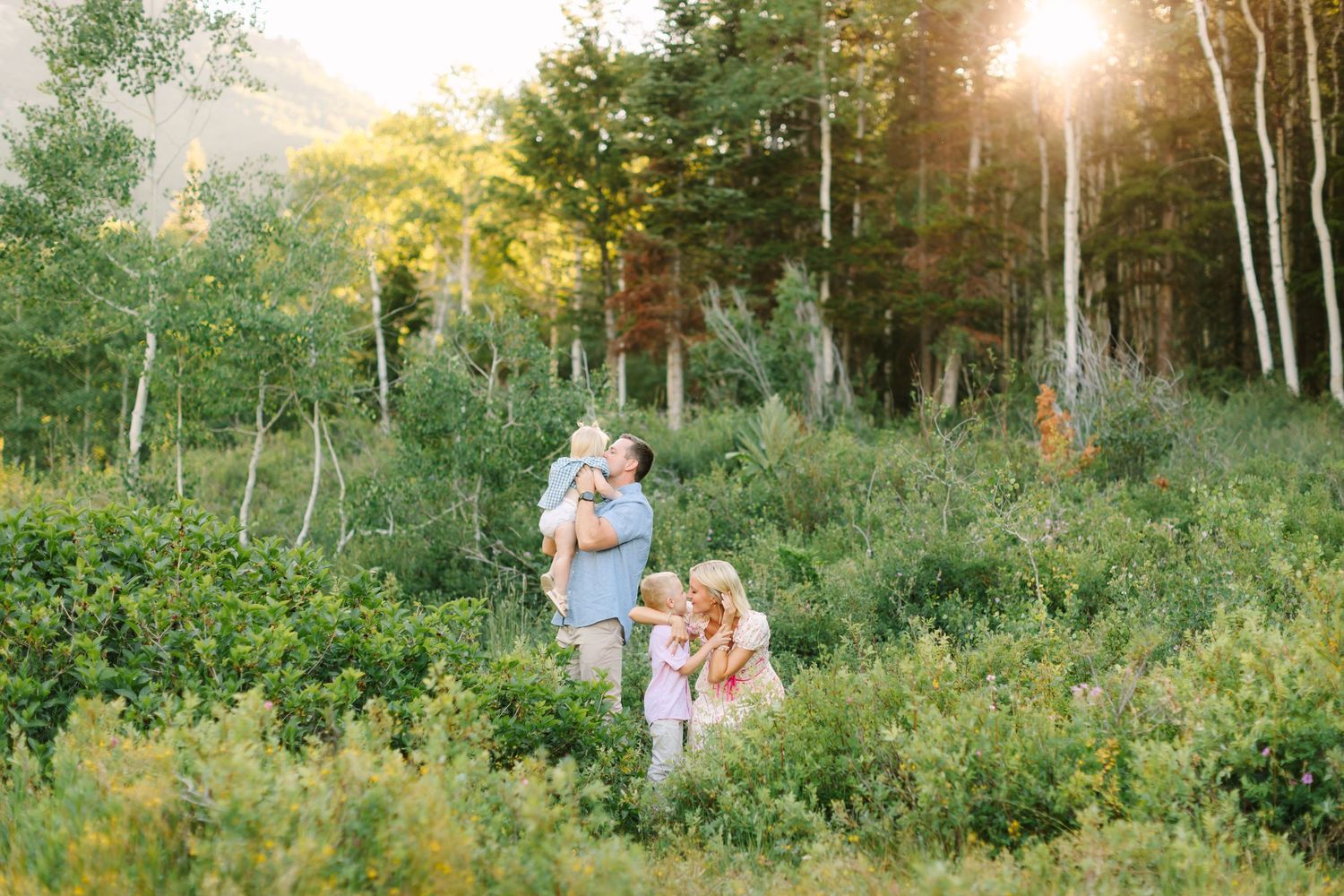 Family enjoying a sunny golden hour moment in a lush green meadow surrounded by aspen trees.