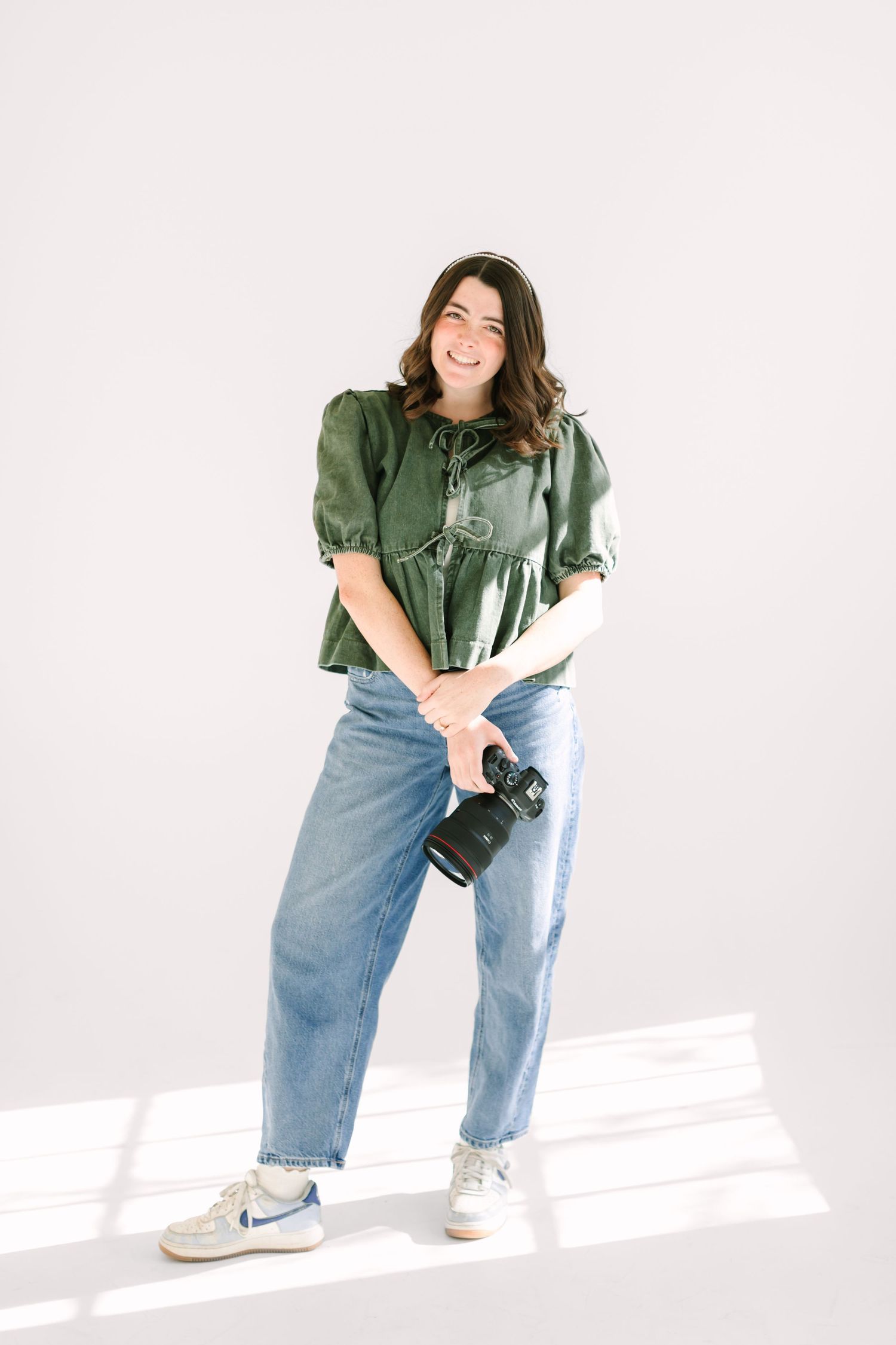 A person in a green button-down shirt and baggy jeans poses playfully against a white studio backdrop.