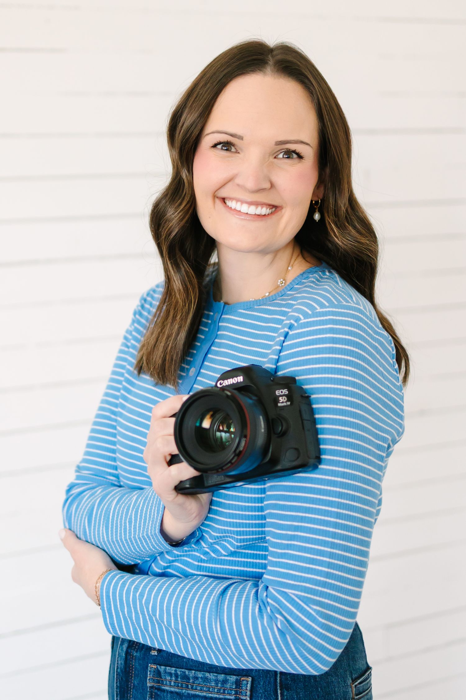 Professional photographer in blue striped shirt holding DSLR camera against white background.