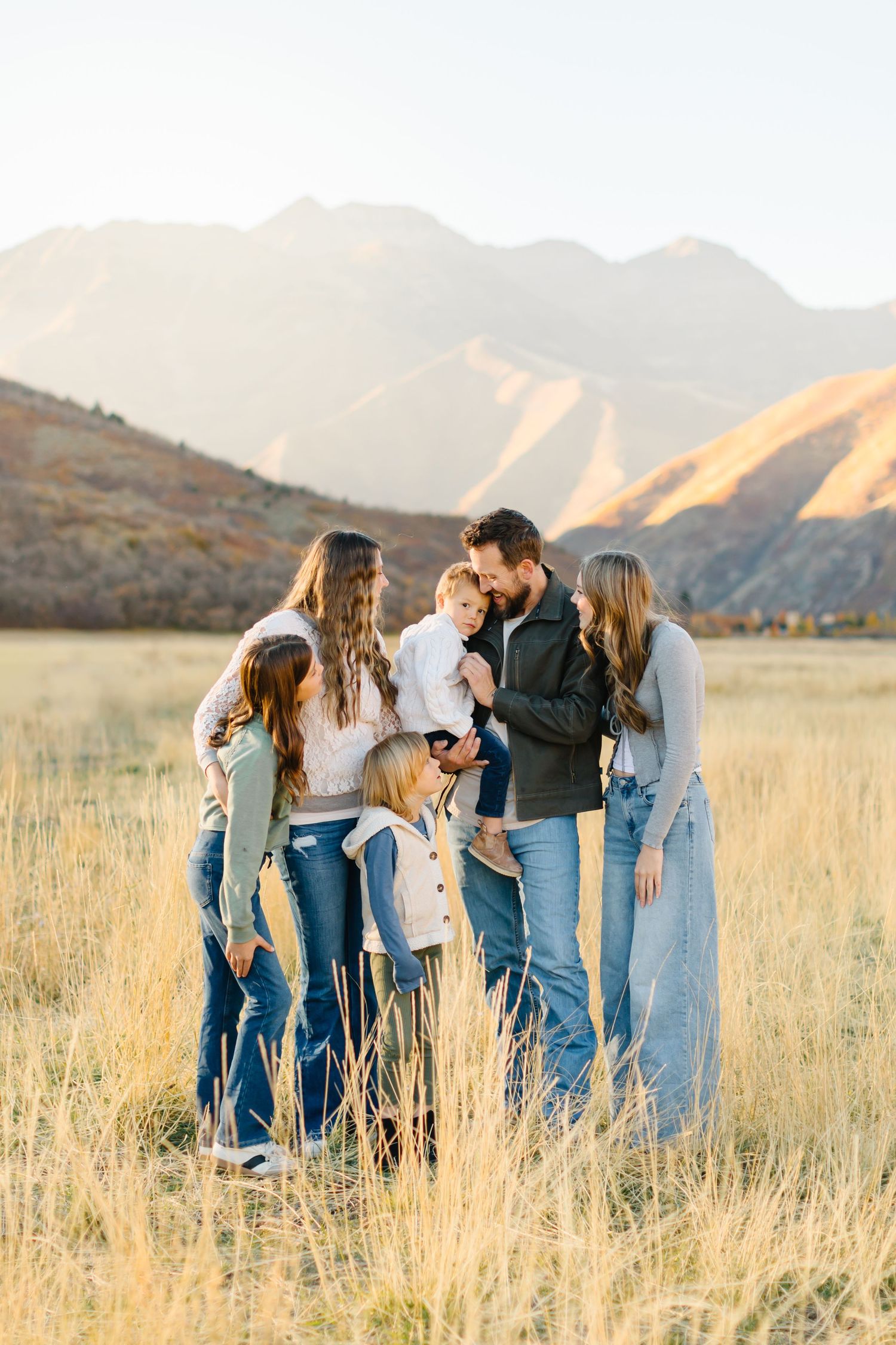 Group in denim poses together in golden field with mountain backdrop at sunset.