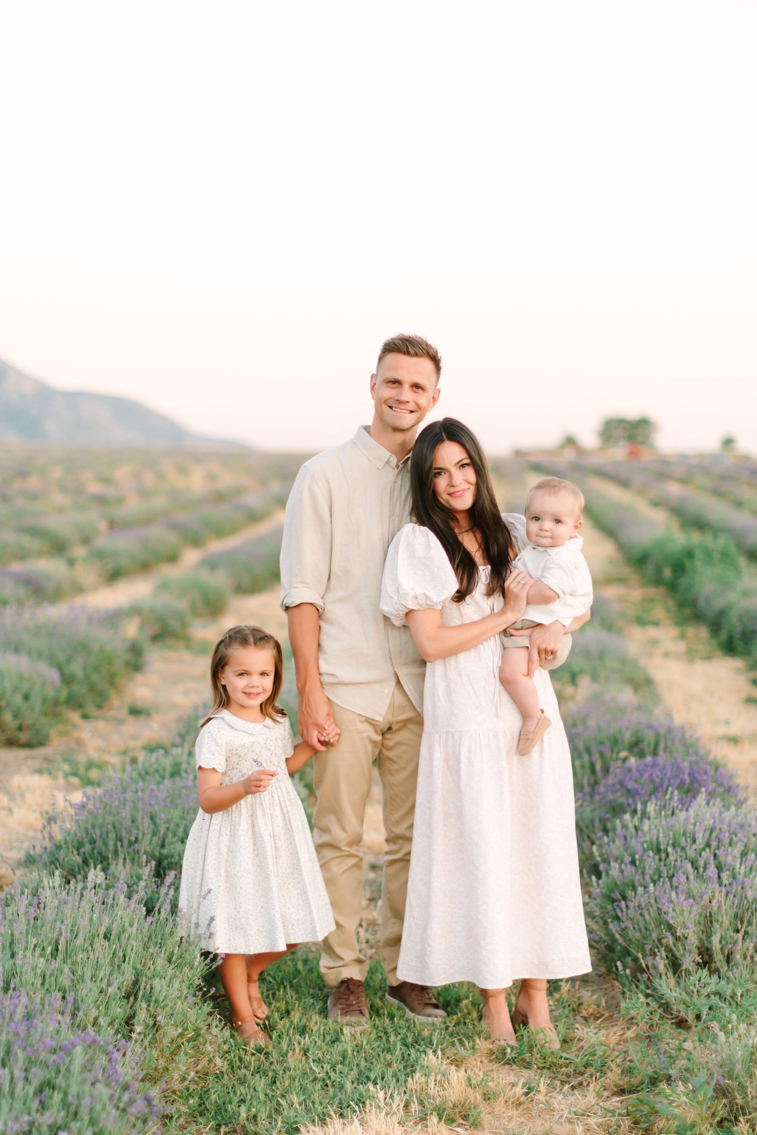 A family poses together in a beautiful lavender field at sunset wearing coordinating white and beige outfits.