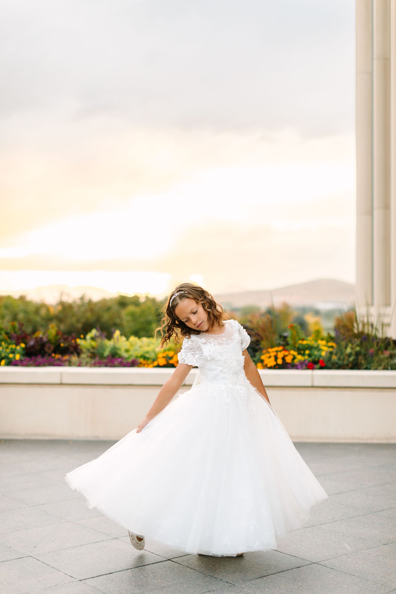 A bride in a flowing white wedding dress twirls gracefully across a balcony at sunset.