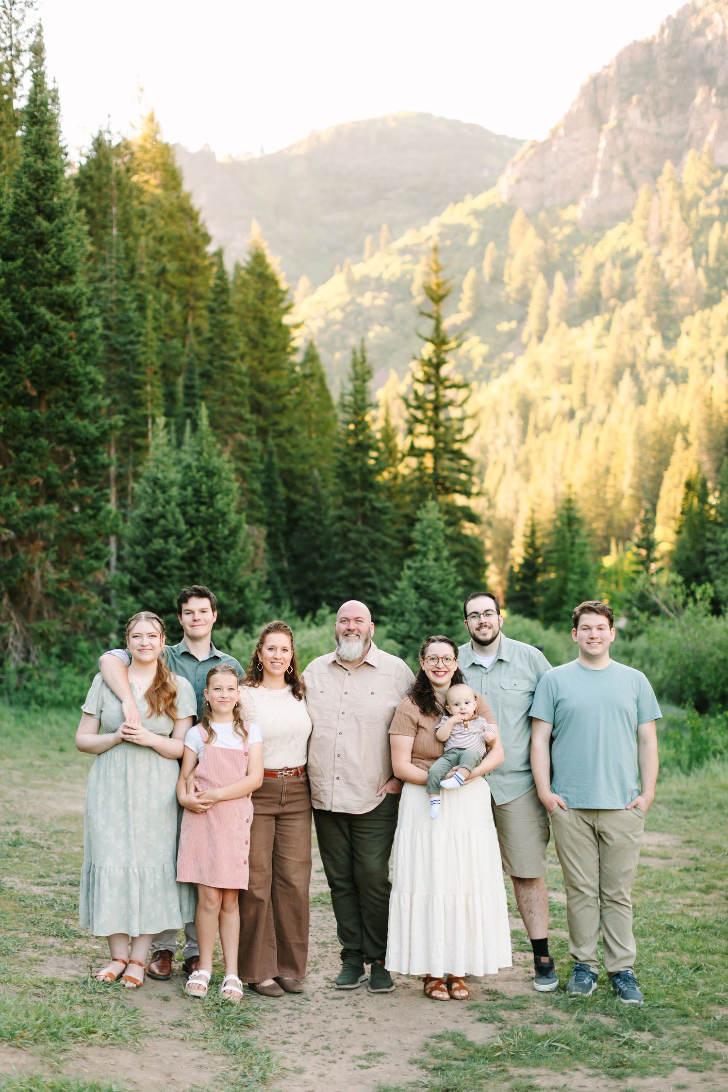 Large family group portrait outdoors in a mountain forest setting during golden hour sunset.