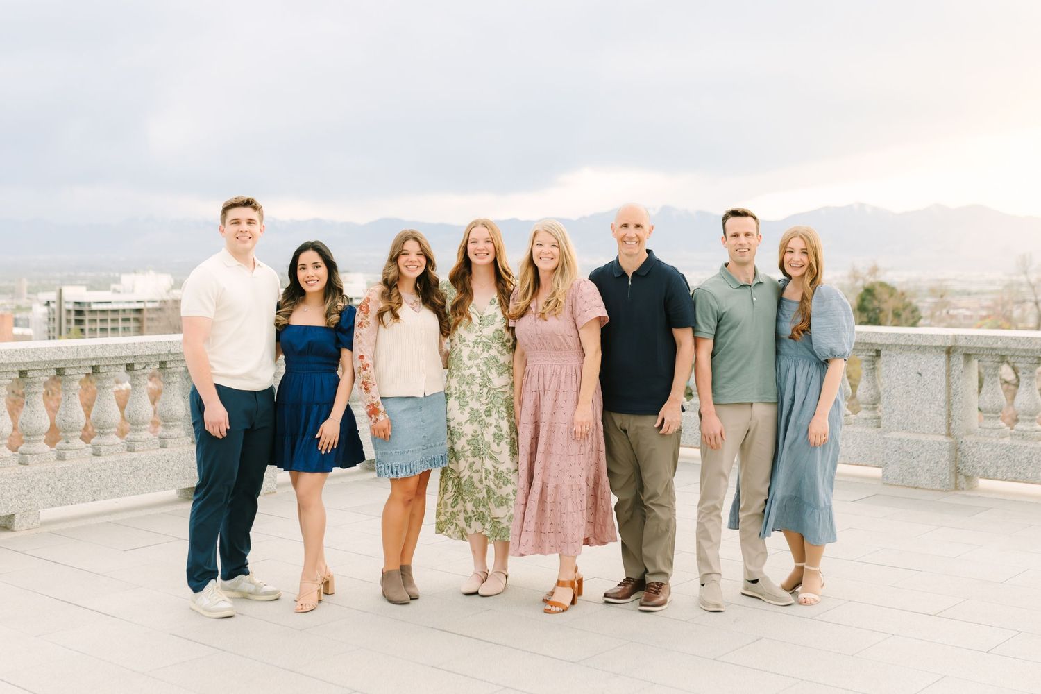 Family of seven posing on a rooftop terrace with mountain views and city skyline in the background.