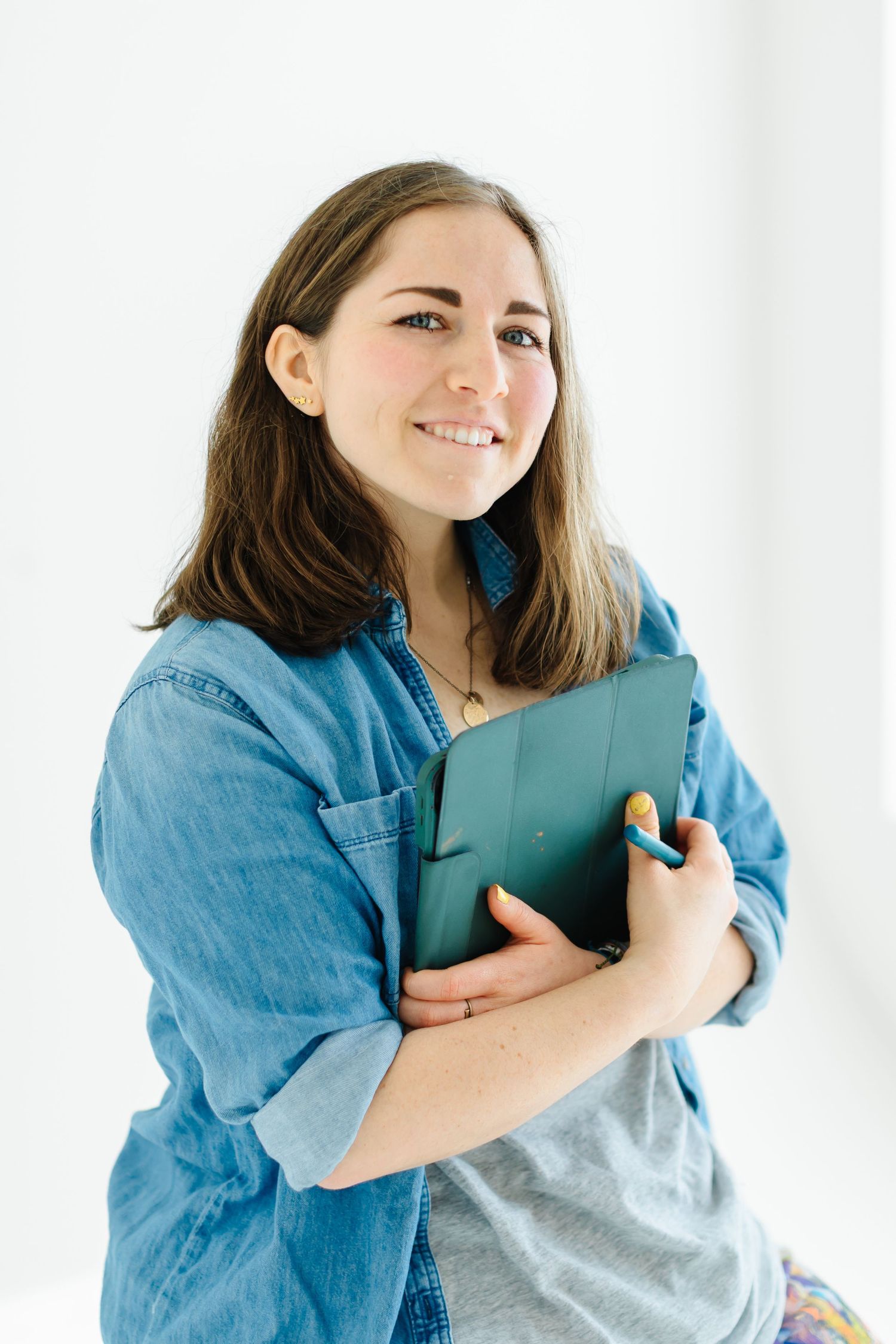 Artist in denim shirt holds teal portfolio against white background at White Space Studio in Provo, Utah in Utah County.