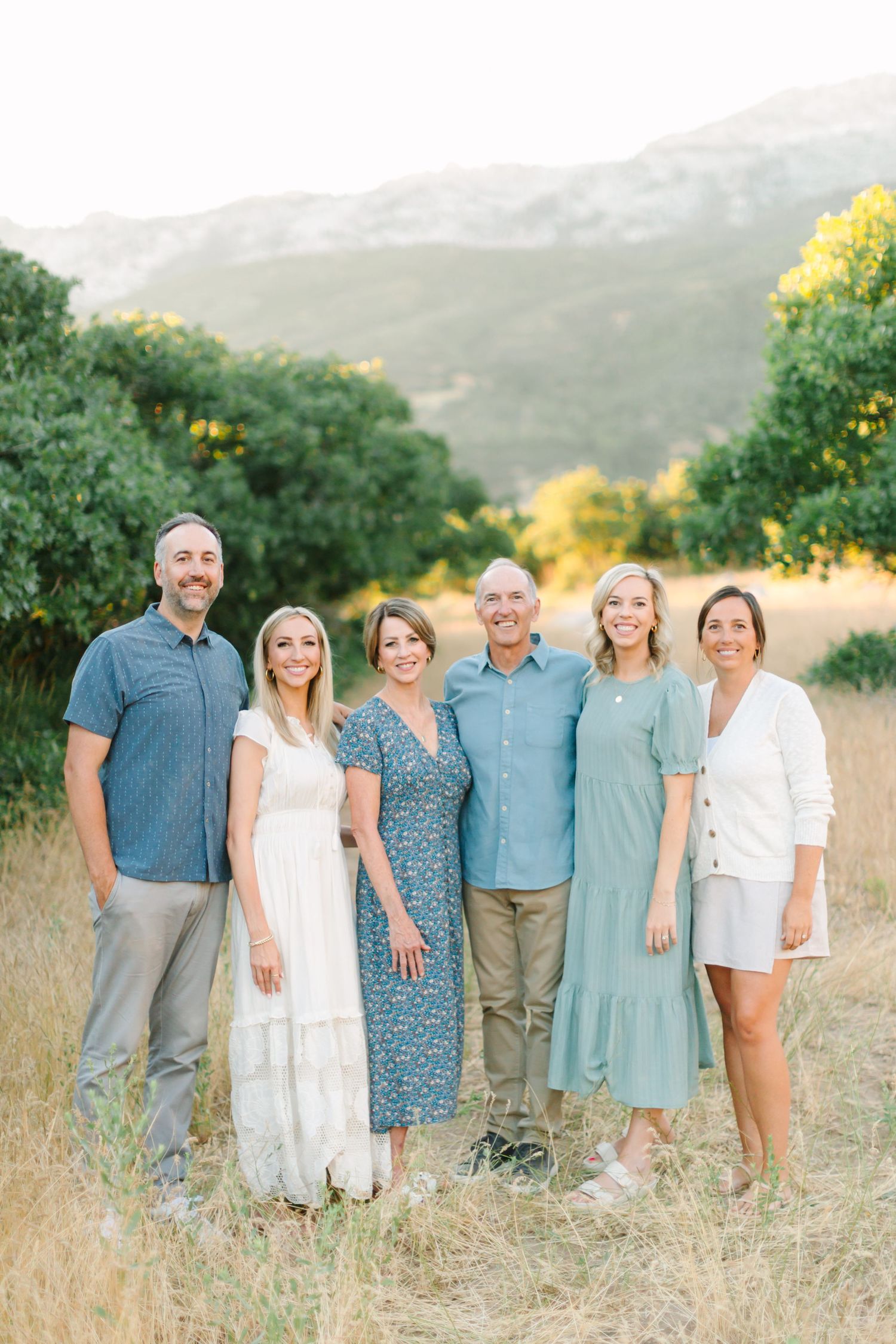 A group stands together in a sun-lit field with rolling hills and greenery in the background during golden hour.