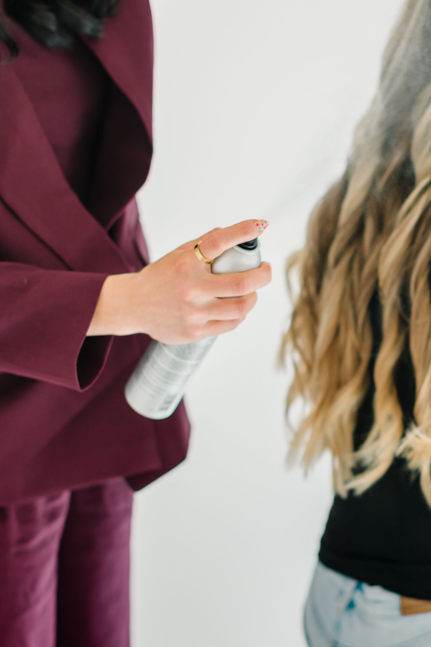 Close-up of hands holding hair styling product while working on blonde hair against white background at White Space Studios in Provo, Utah .