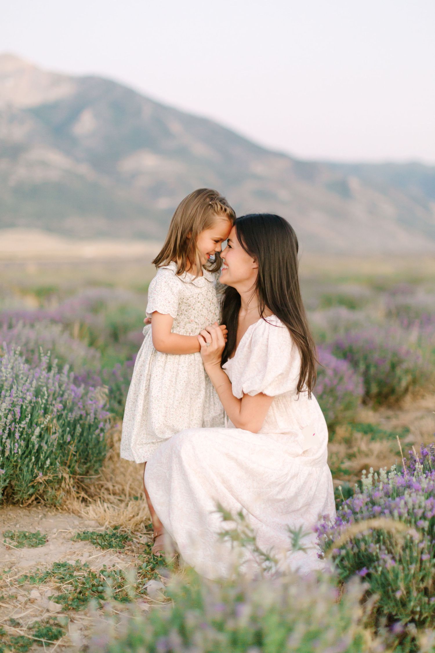 A mother and daughter share tender moments in a blooming lavender field with mountains in the background.