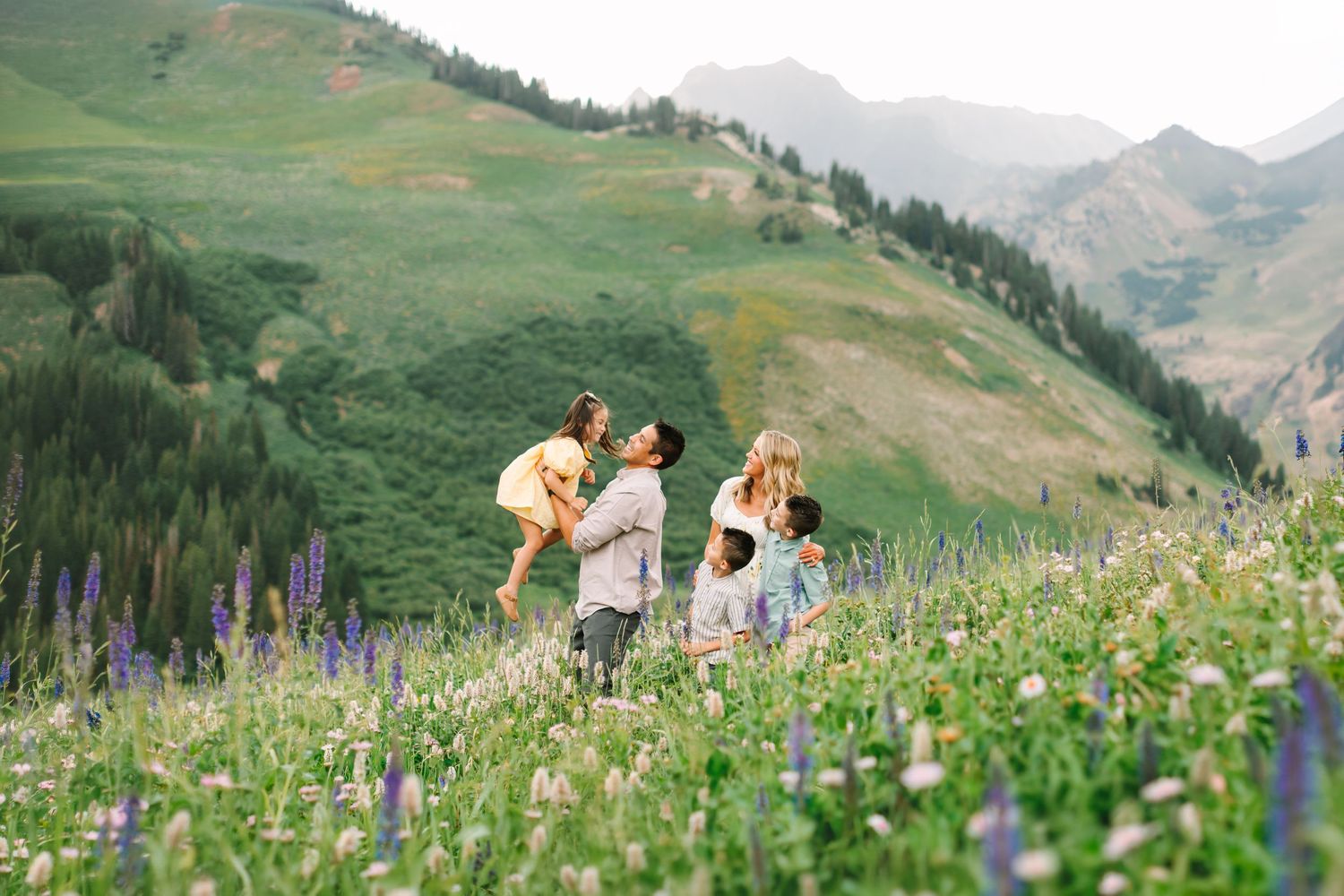 Family playing in a wildflower meadow with lush green mountains in the background on a sunny day at Albion Basin in Utah.