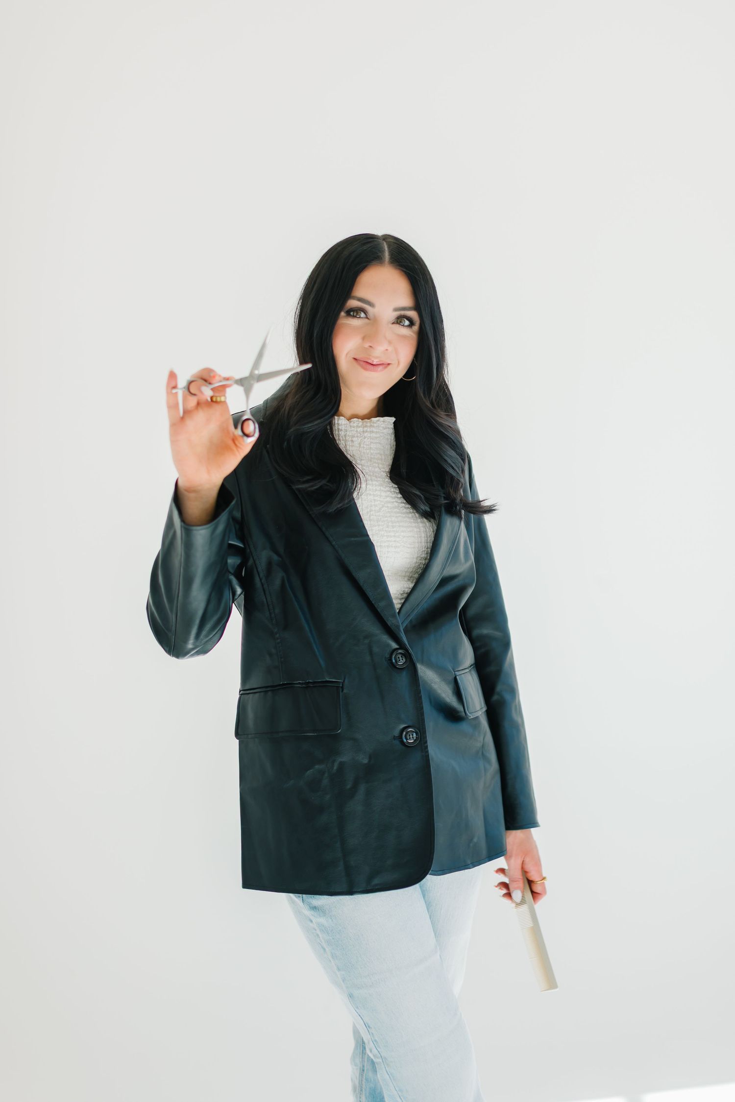 Professional hairstylist in black blazer holding styling tool against white background at White Space Studios in Provo, Utah in Utah County.
