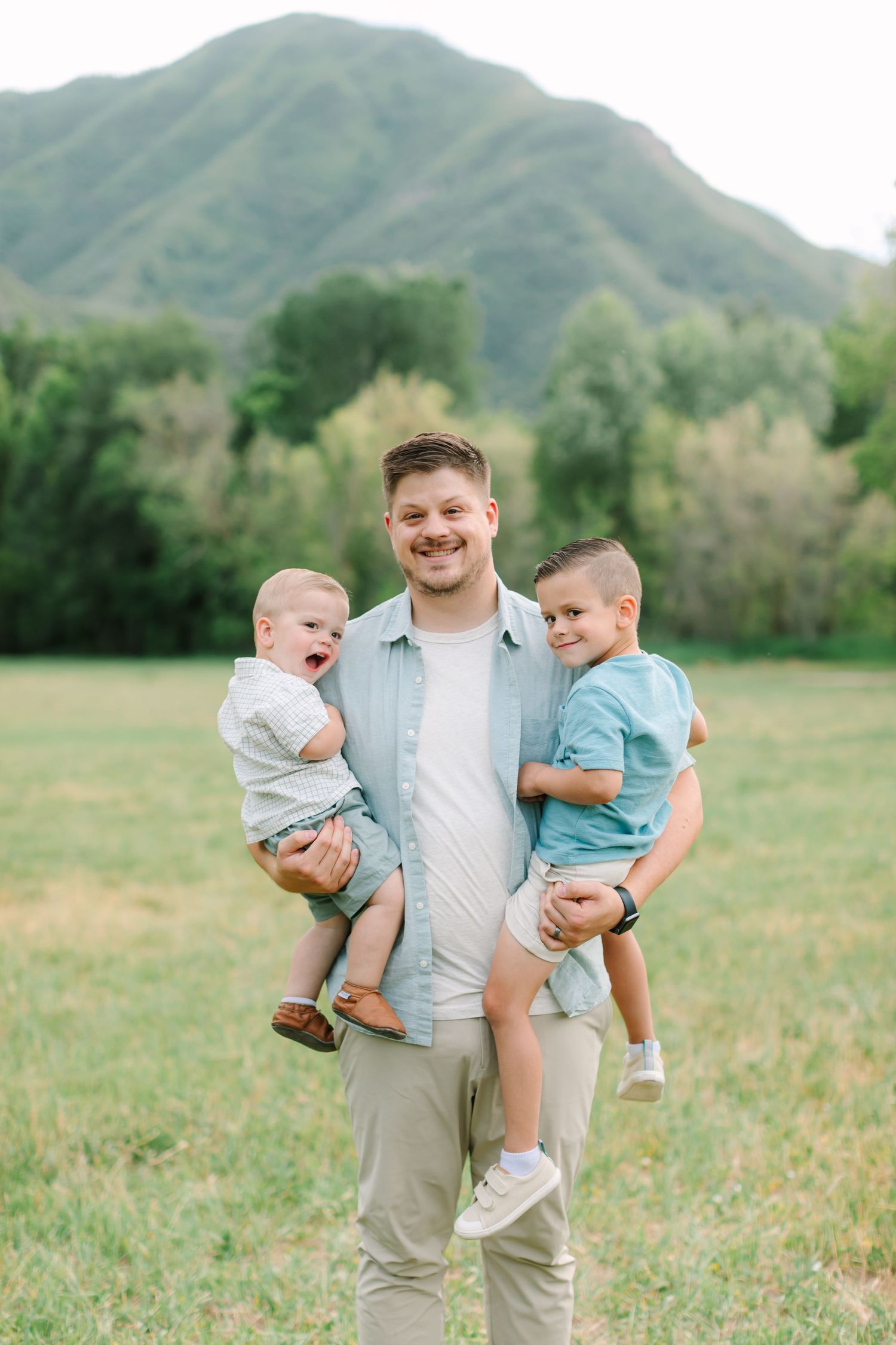A joyful family moment captured in a grassy field with mountains in the background.