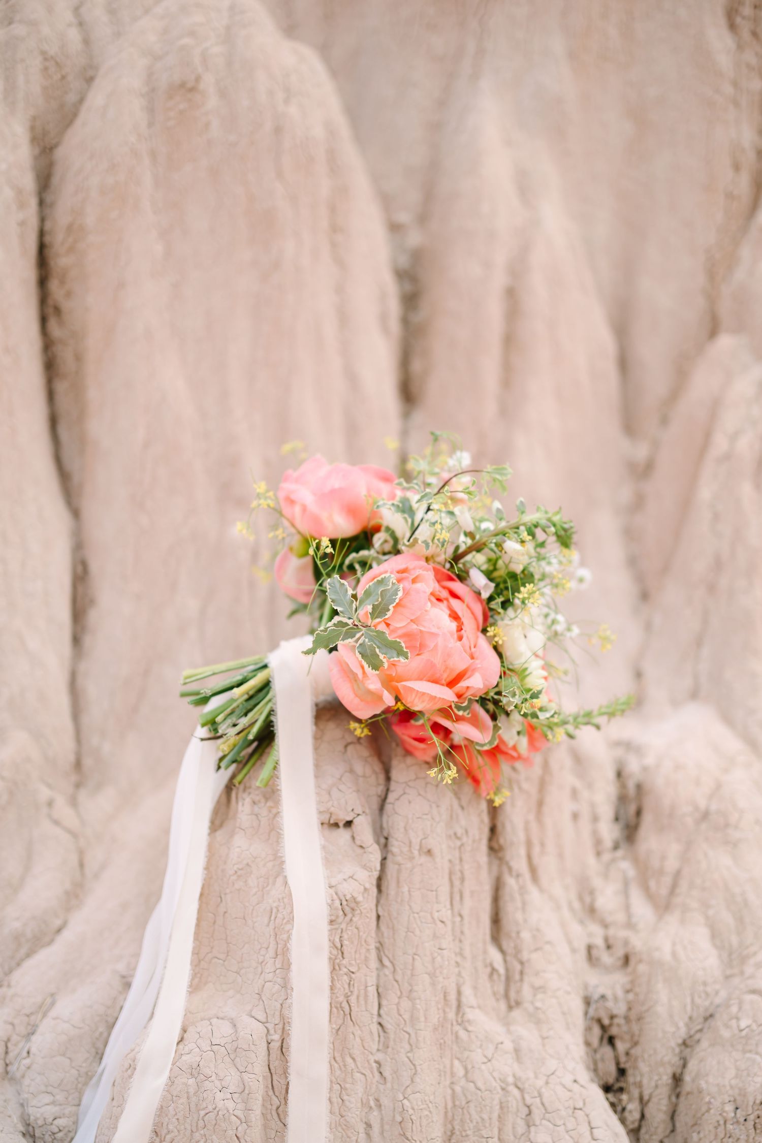 A delicate coral pink bridal bouquet with roses and baby's breath rests against a textured beige stone background.