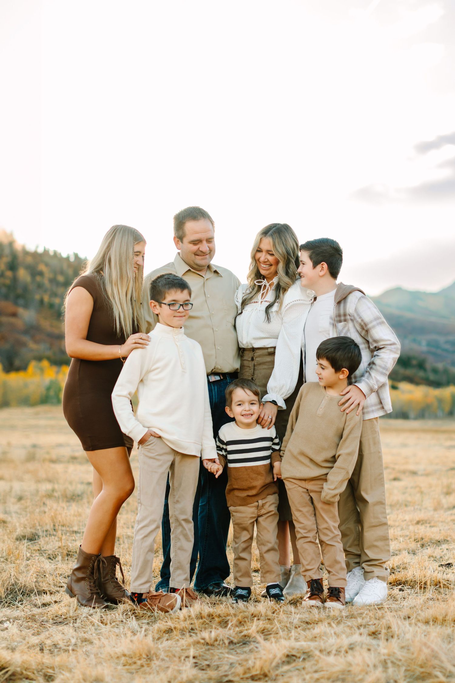 A family group stands together in a grassy field with mountains and autumn foliage in the background.