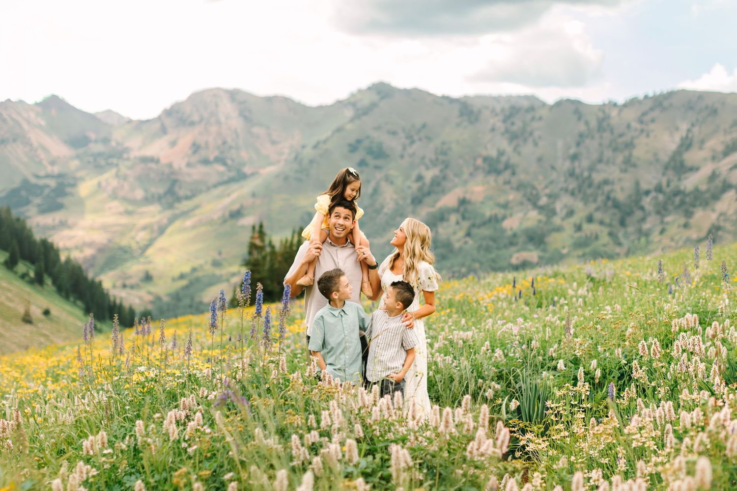Family of five posing in a wildflower meadow with mountain backdrop on a cloudy day.