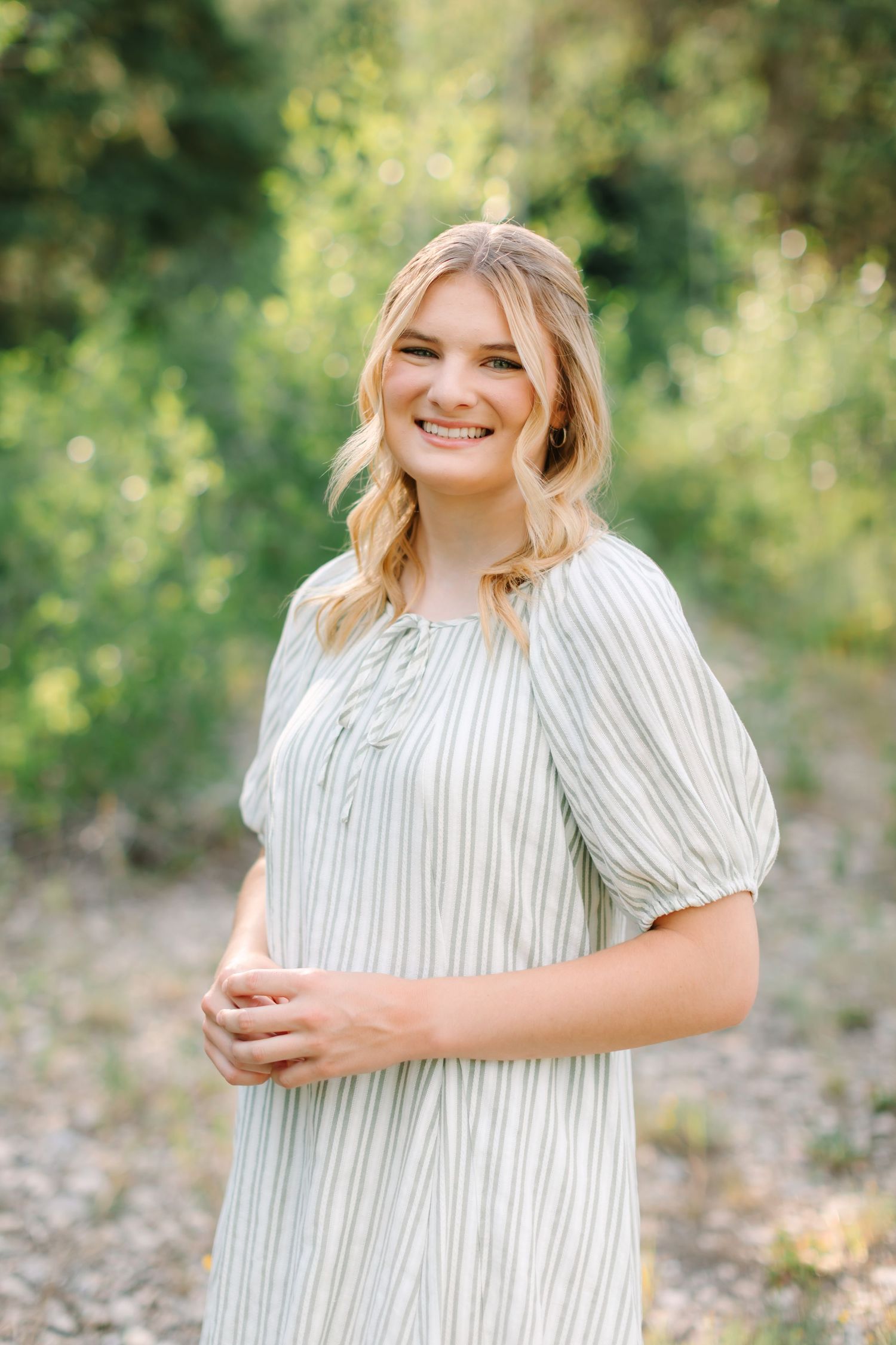 Large family group smiling outdoors in coordinated sage green and white outfits with lush green trees behind in Provo, Utah.