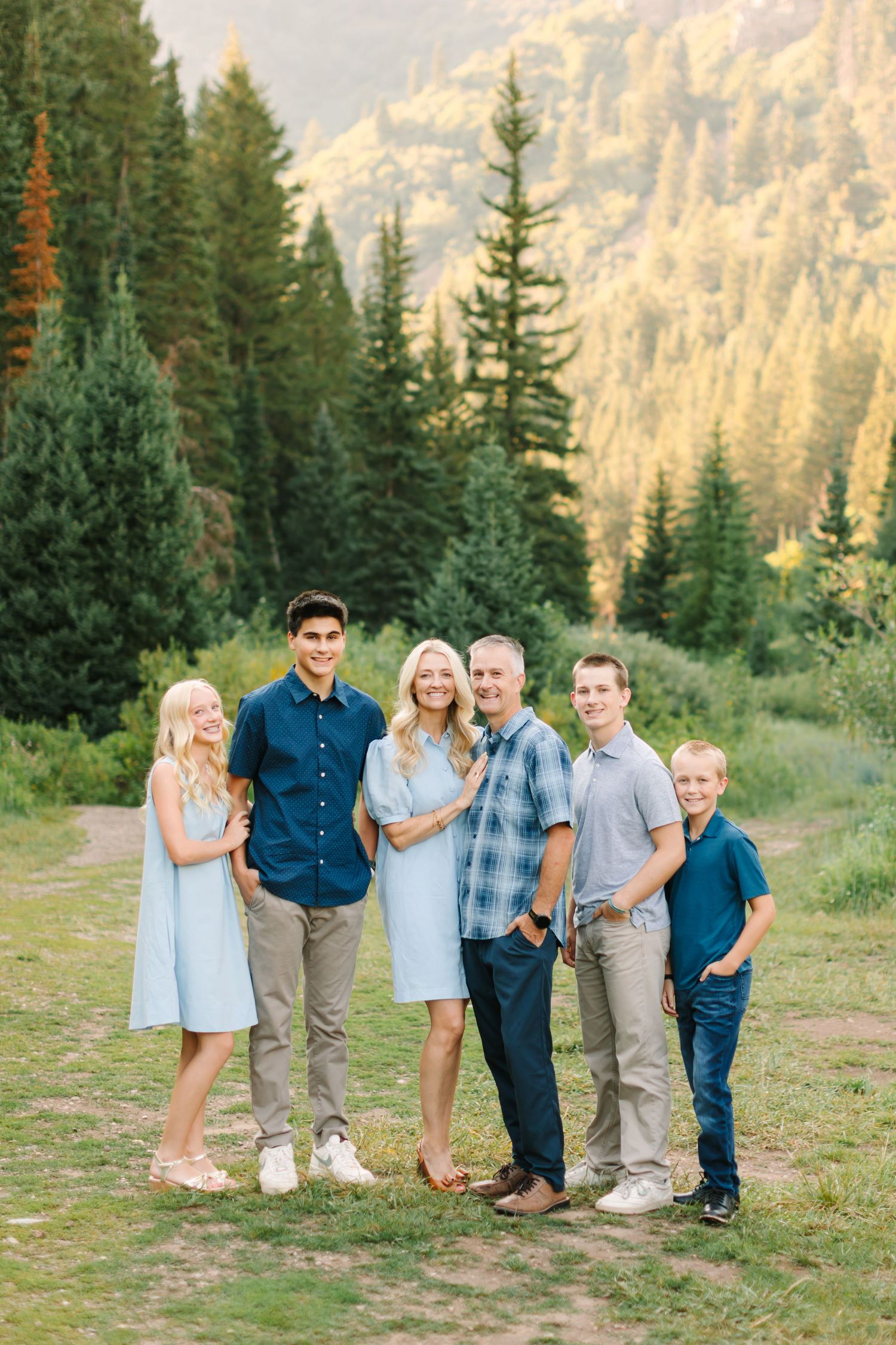 Family of six posing outdoors in a meadow surrounded by tall pine trees during golden hour in Salt Lake, Utah.