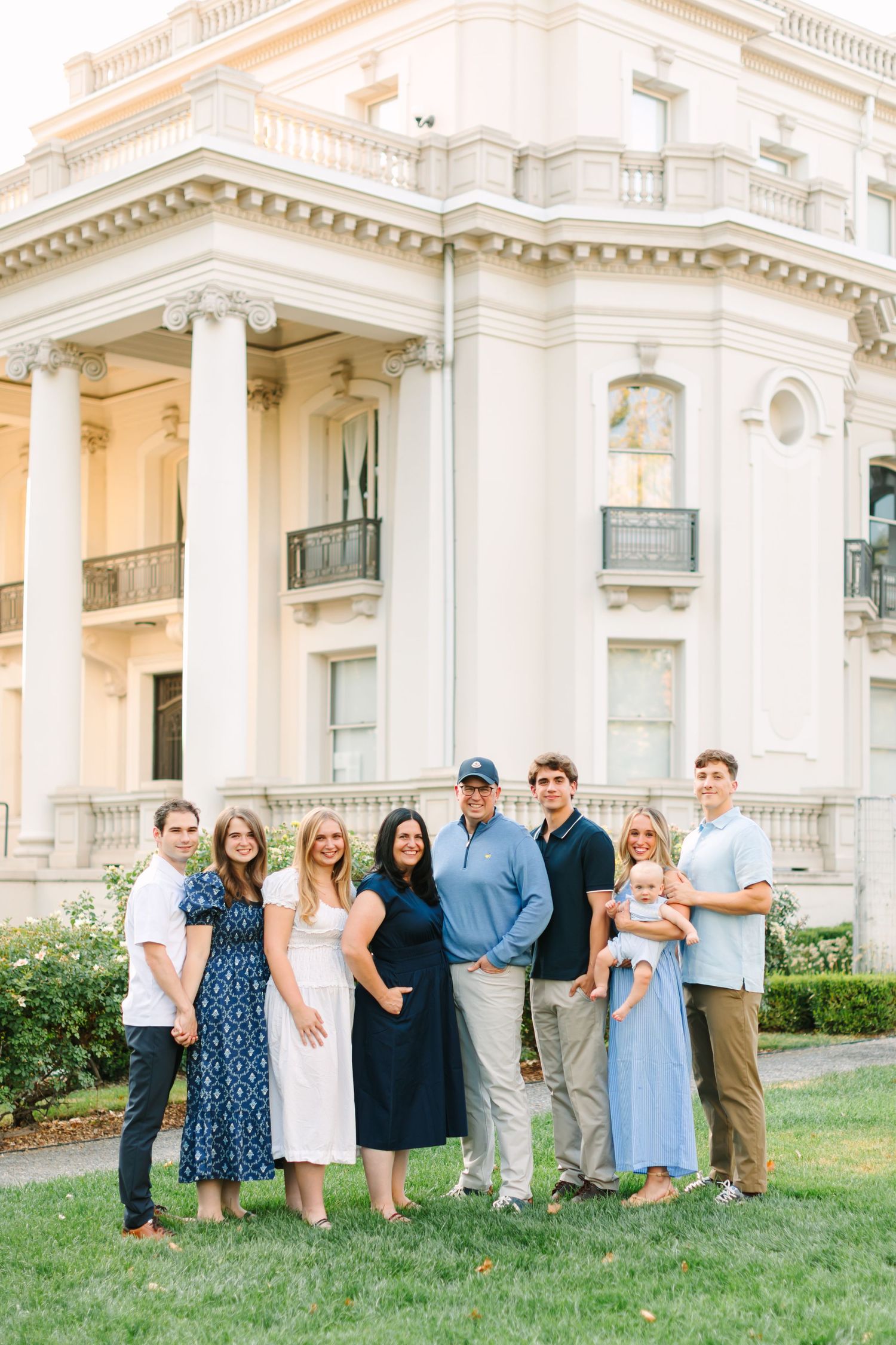 Large family group portrait on lawn in front of elegant white neoclassical mansion with columns.