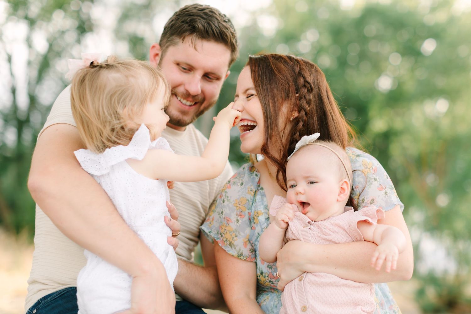 Happy family with two young children laughing and smiling together outdoors in a bright, green natural setting.