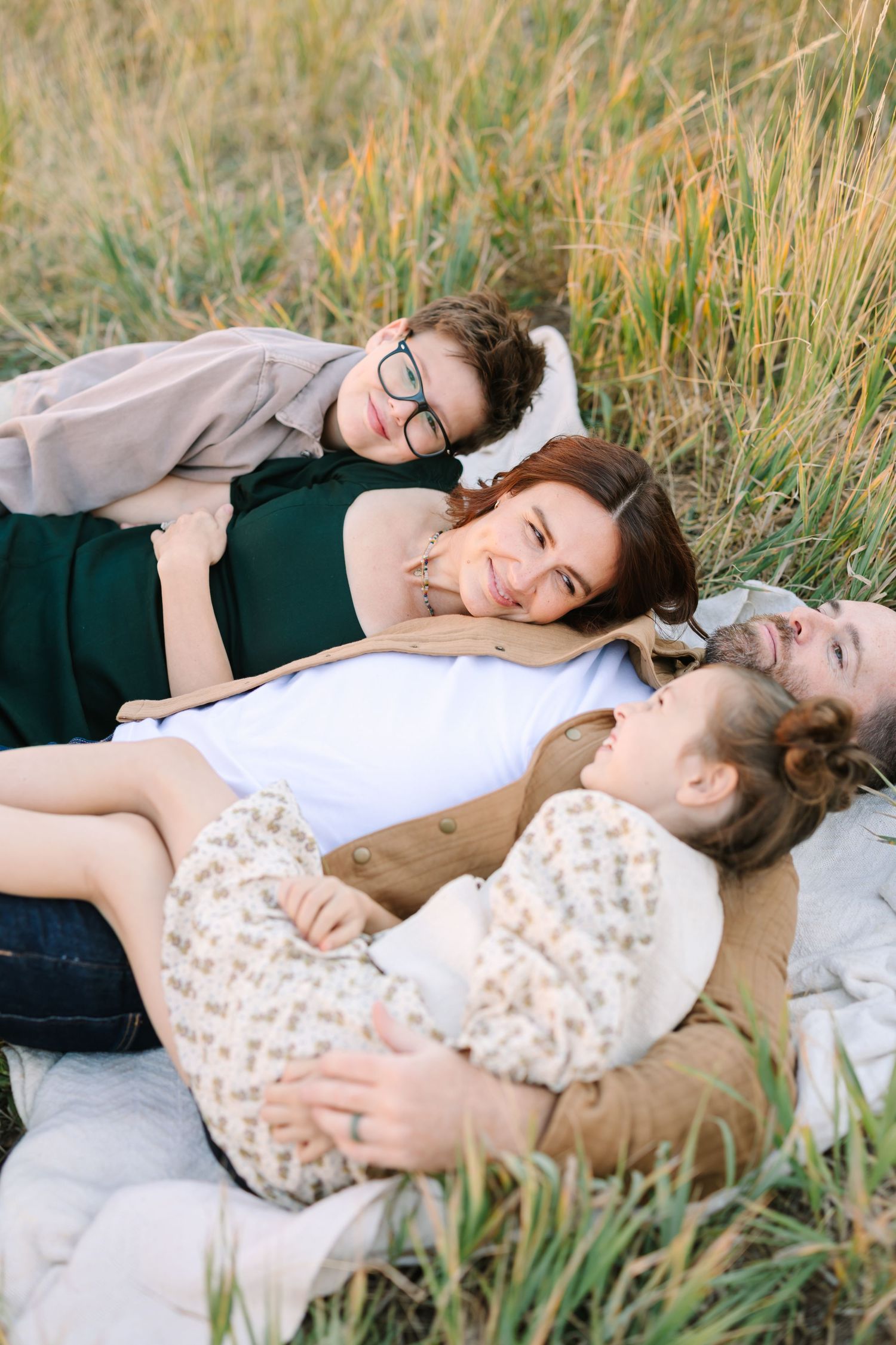 Couple lying together on a blanket in tall grass during a romantic outdoor photoshoot.