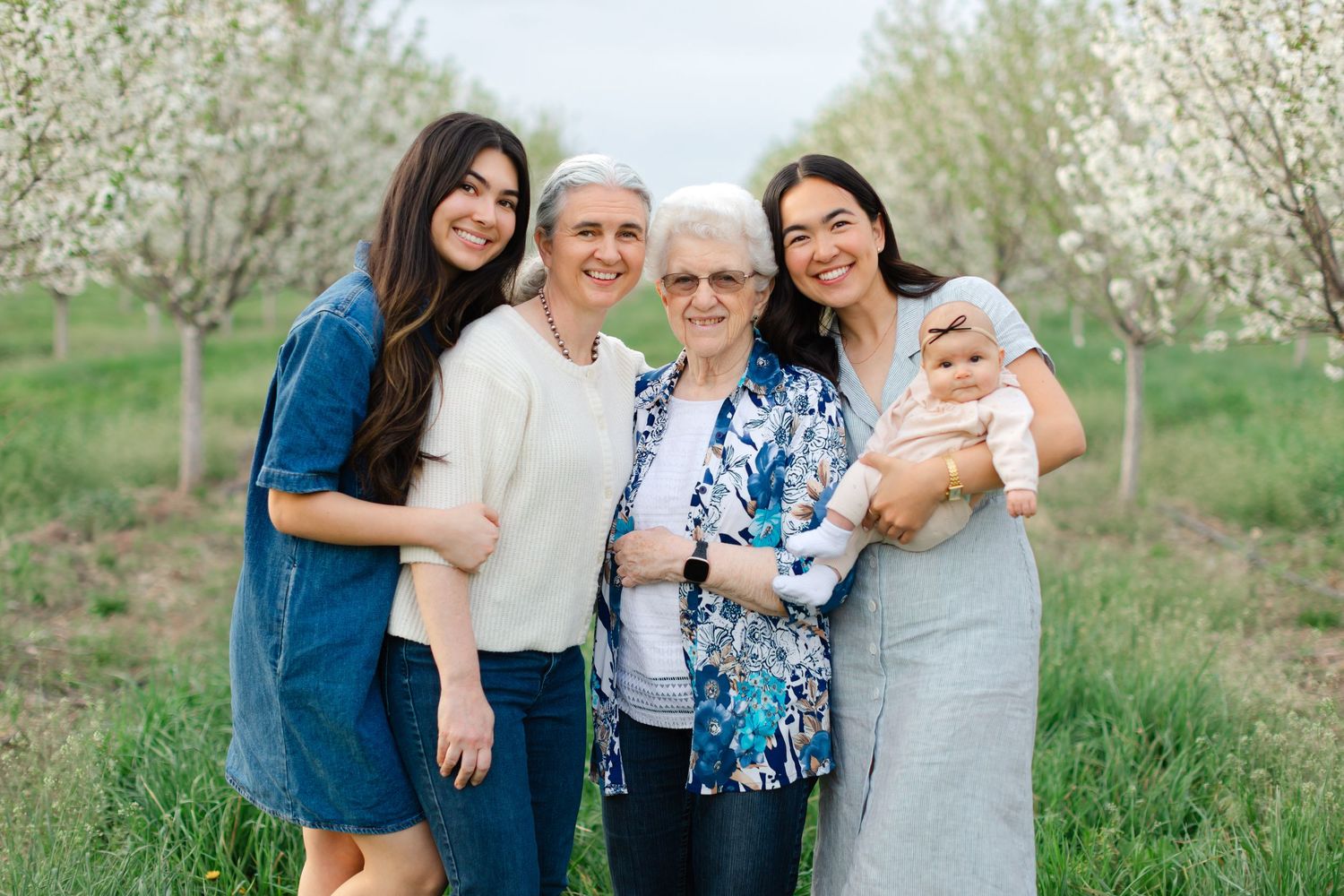 A multi-generational family poses together in a blooming spring orchard with white flowers in the background.