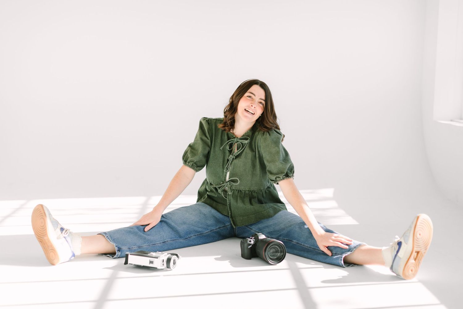 A person in a green shirt and jeans sits casually on a white floor in various relaxed poses.