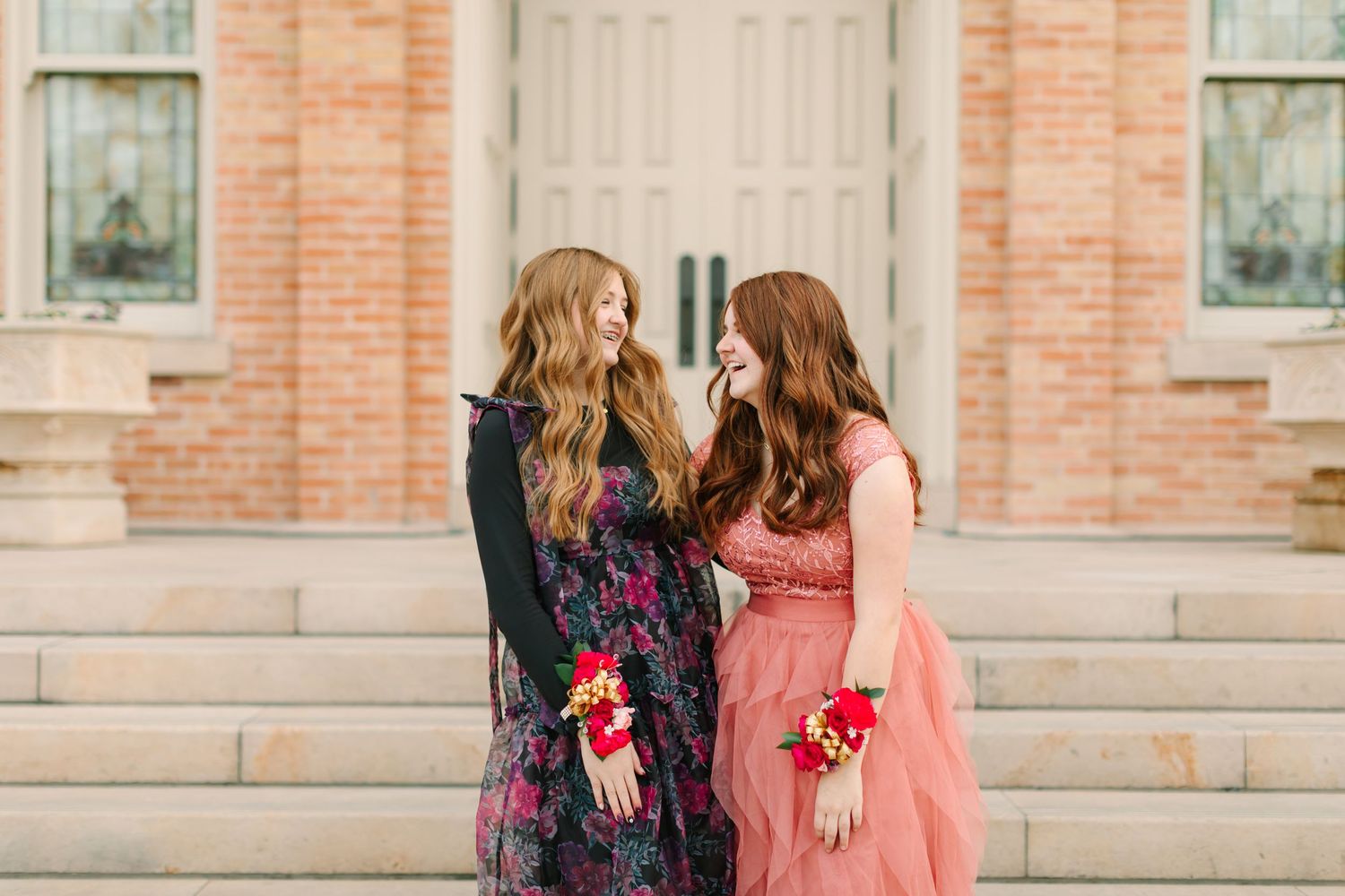 Two people in coordinating pink and navy outfits walk together along a brick building exterior.