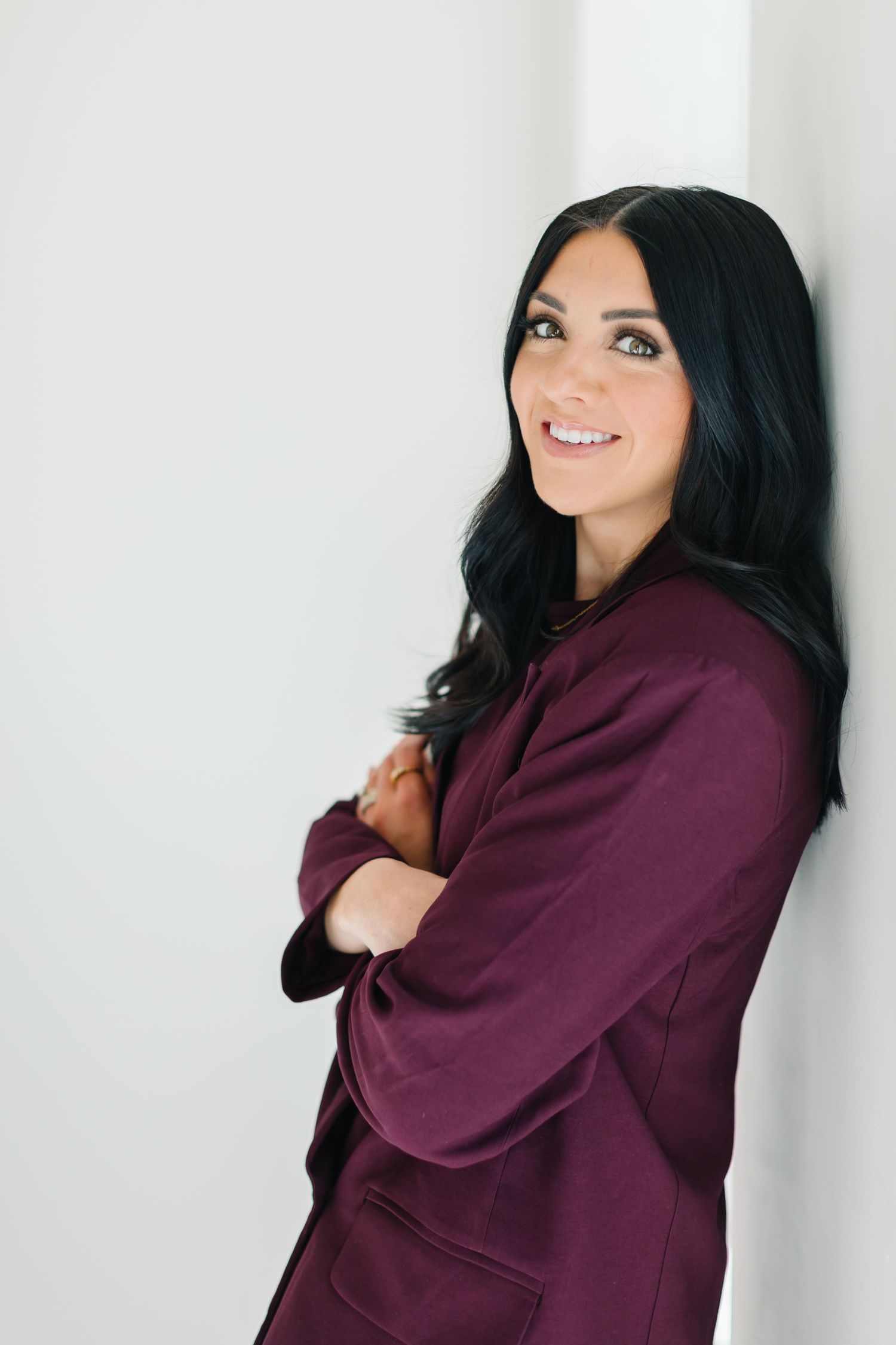 Person in burgundy suit poses against white wall showing different expressions and angles at White Space Studios in Provo, Utah in Utah Cou.