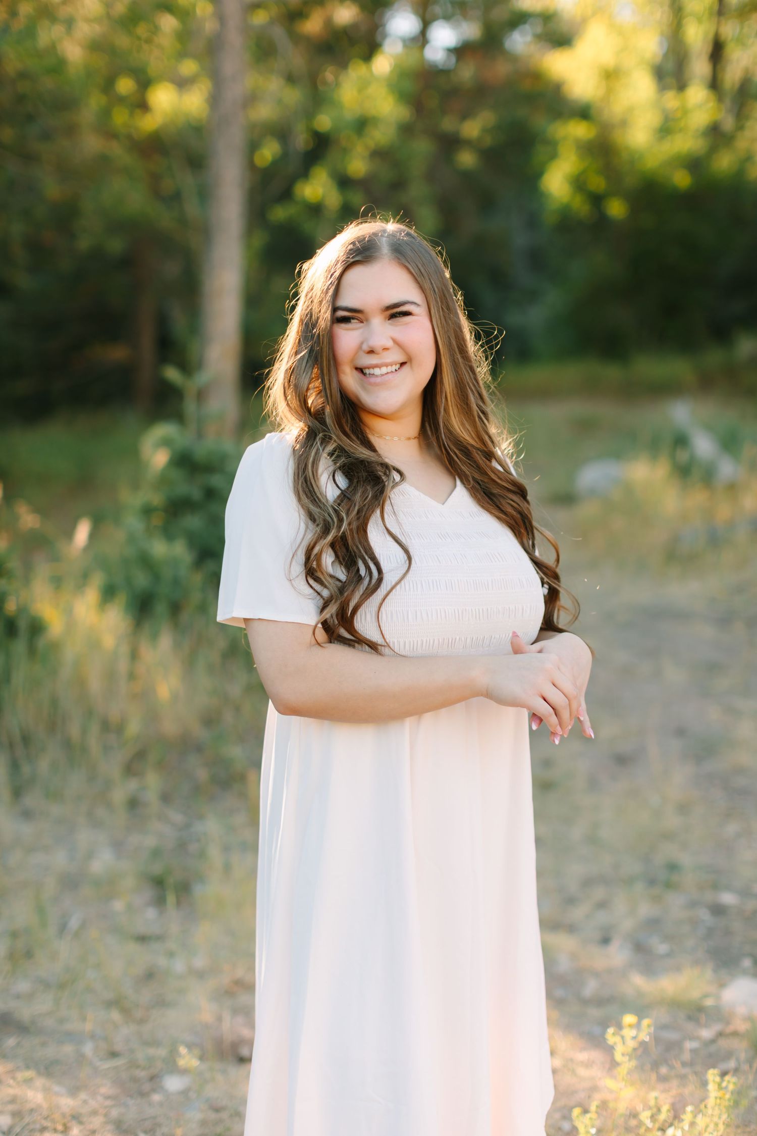 A high school senior stands against green foliage for her high school graduation photoshoot in American Fork, Utah in Utah County.