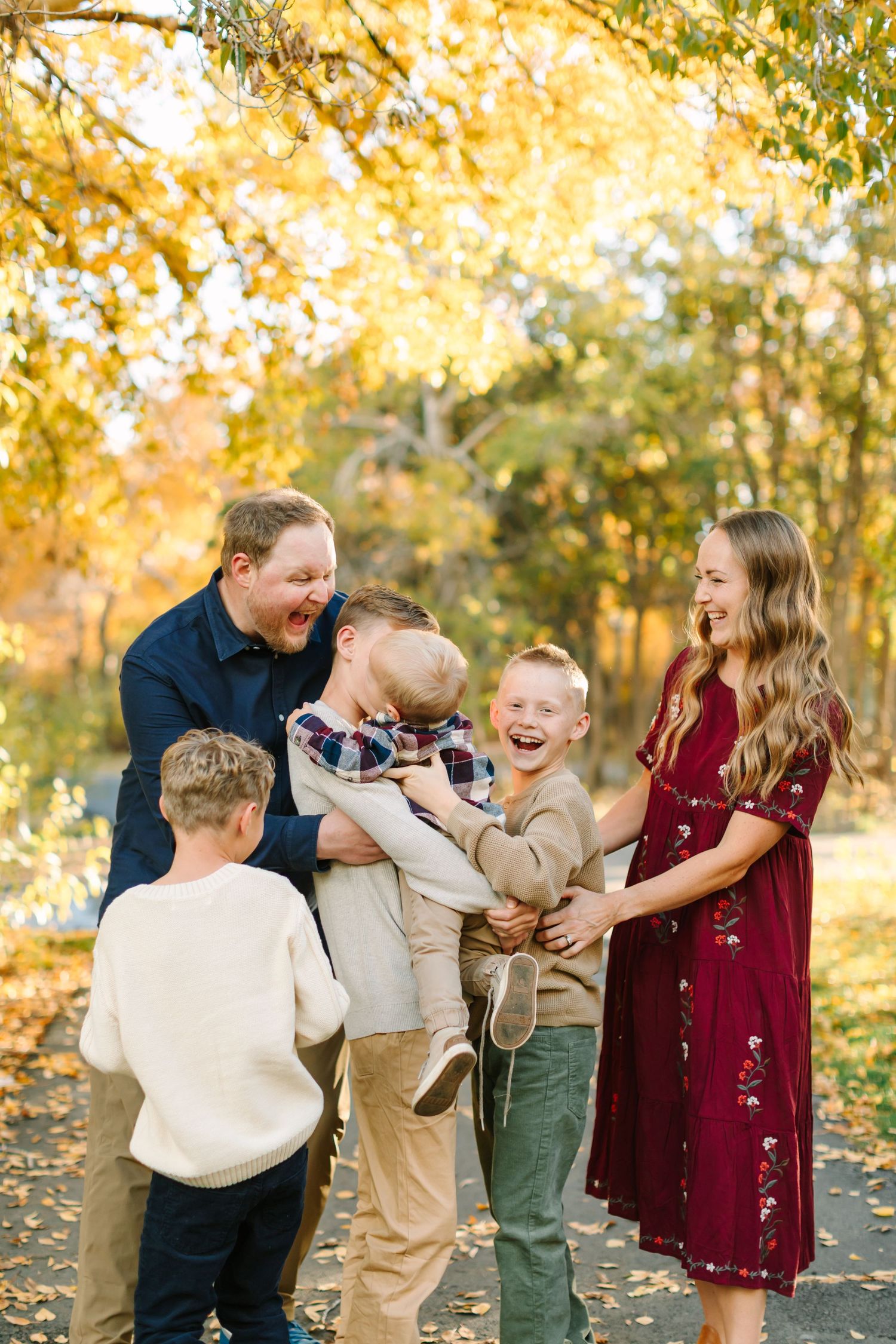 Family shares candid laughter and joy during golden hour autumn photo session in park setting.