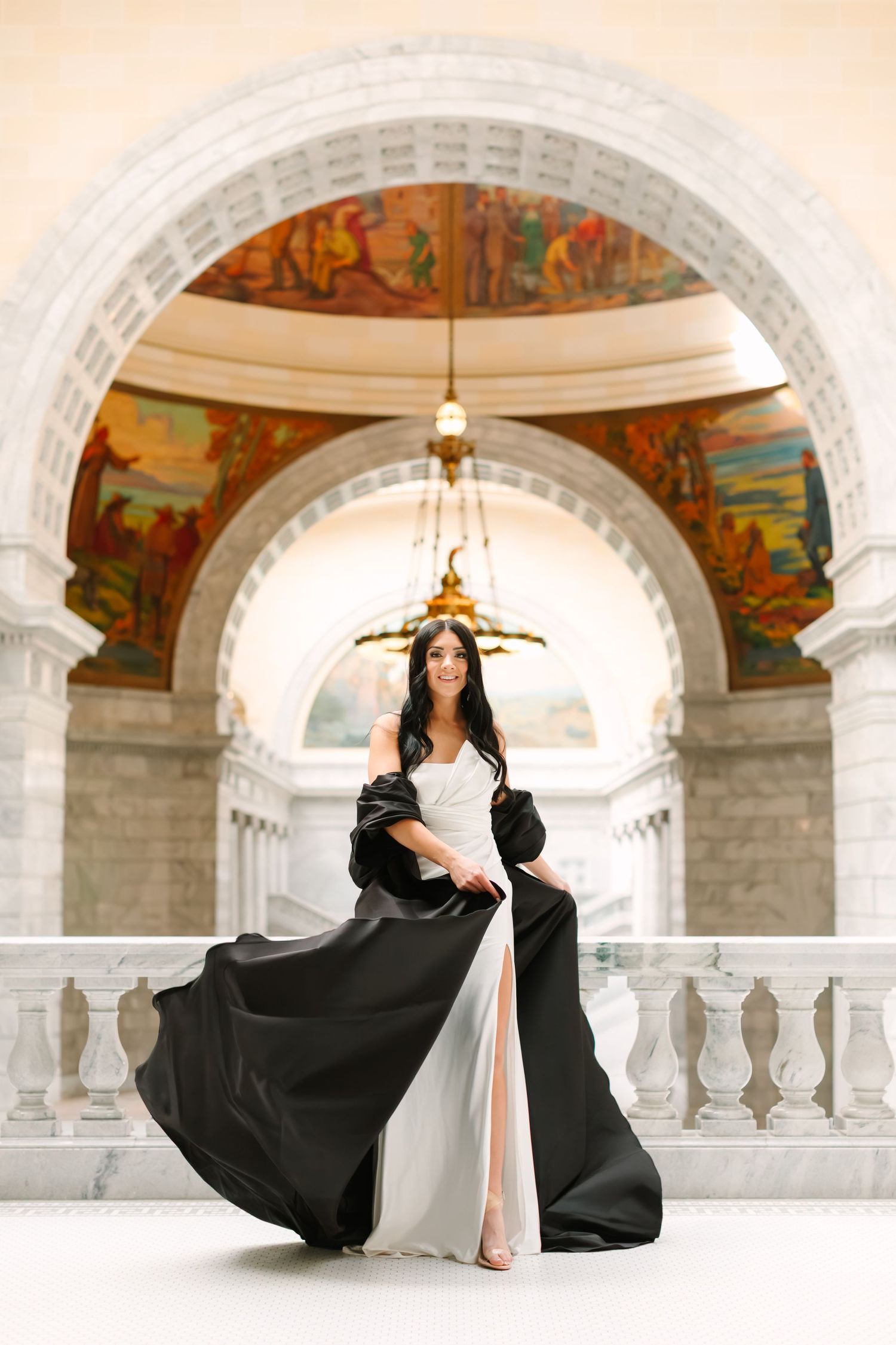 A flowing black dress twirls gracefully under ornate arched columns with painted murals and elegant architecture.