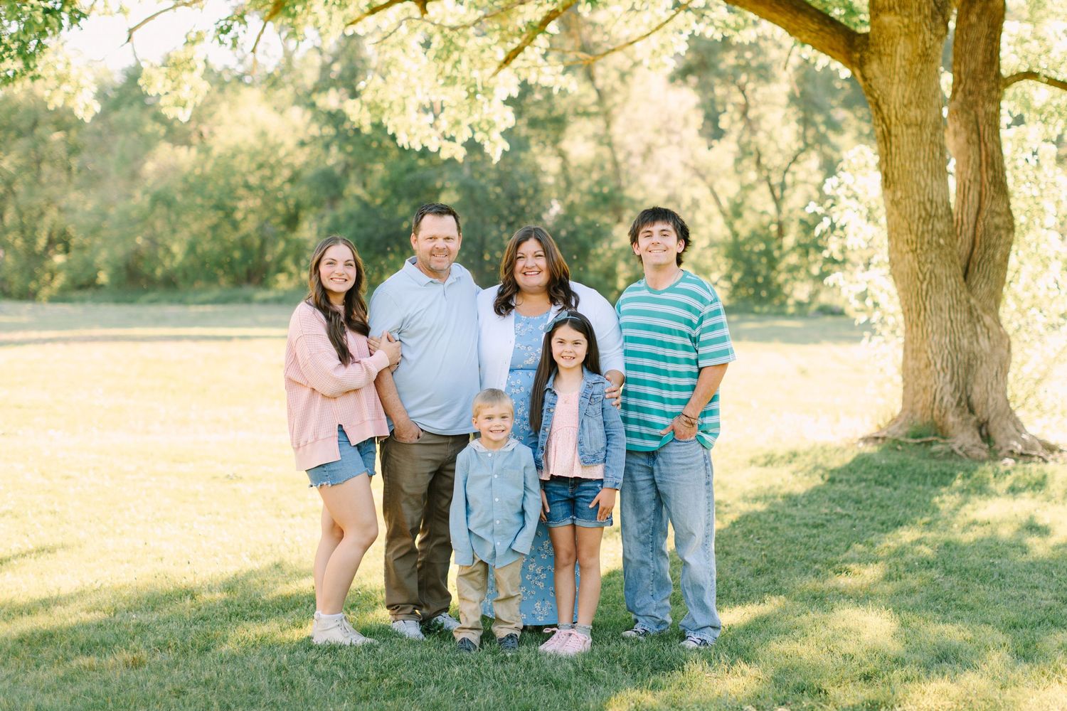 A group stands together outdoors under a large tree during a sunny afternoon photo session.