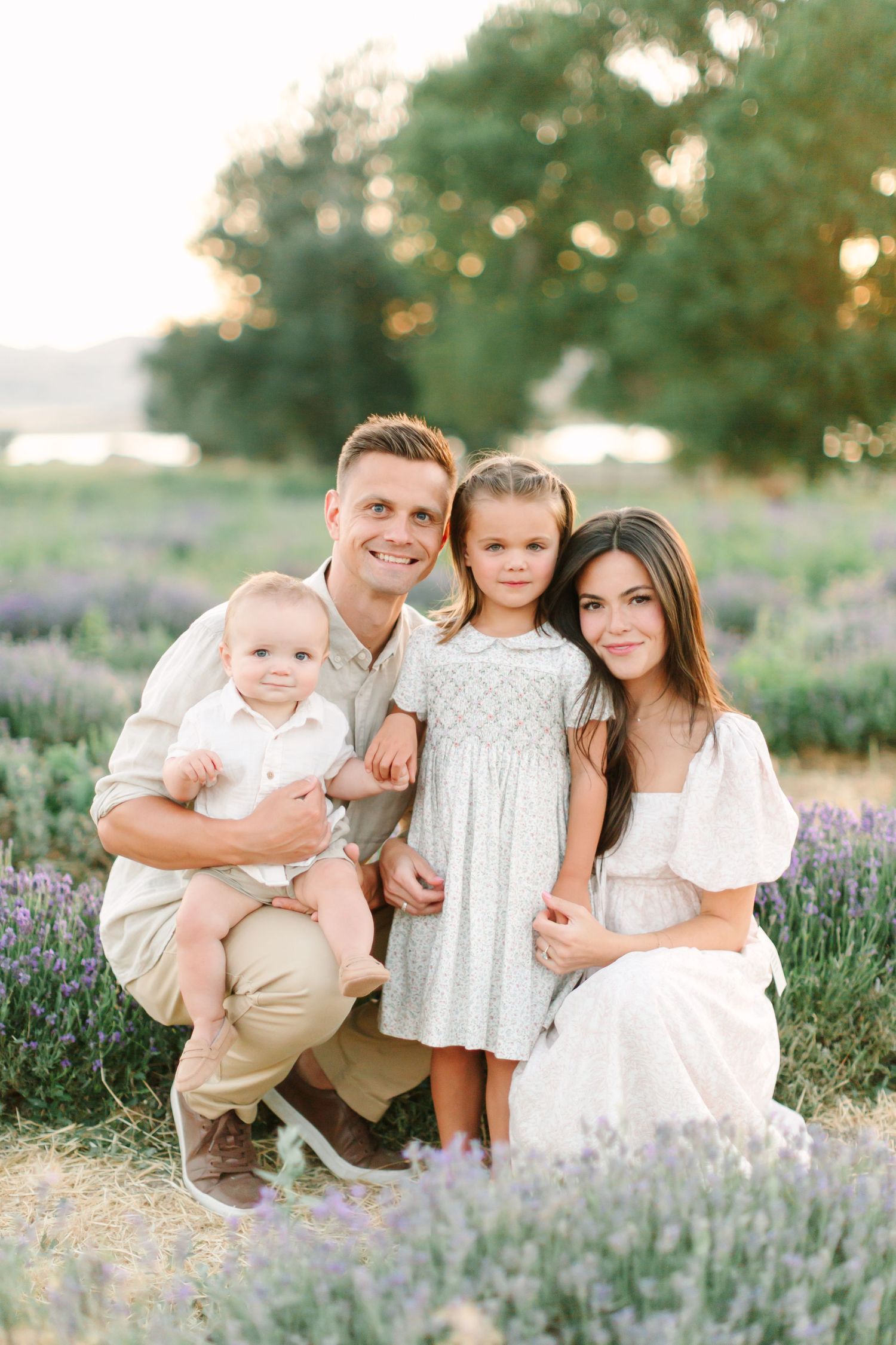 A family poses for portraits among purple wildflowers in a sunlit meadow at sunset.