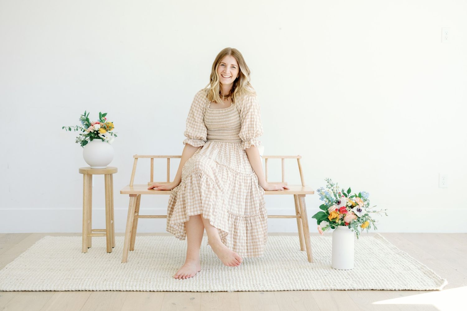 Elegant maternity photo series in soft beige tones against white backdrop with floral accents and wooden furniture.