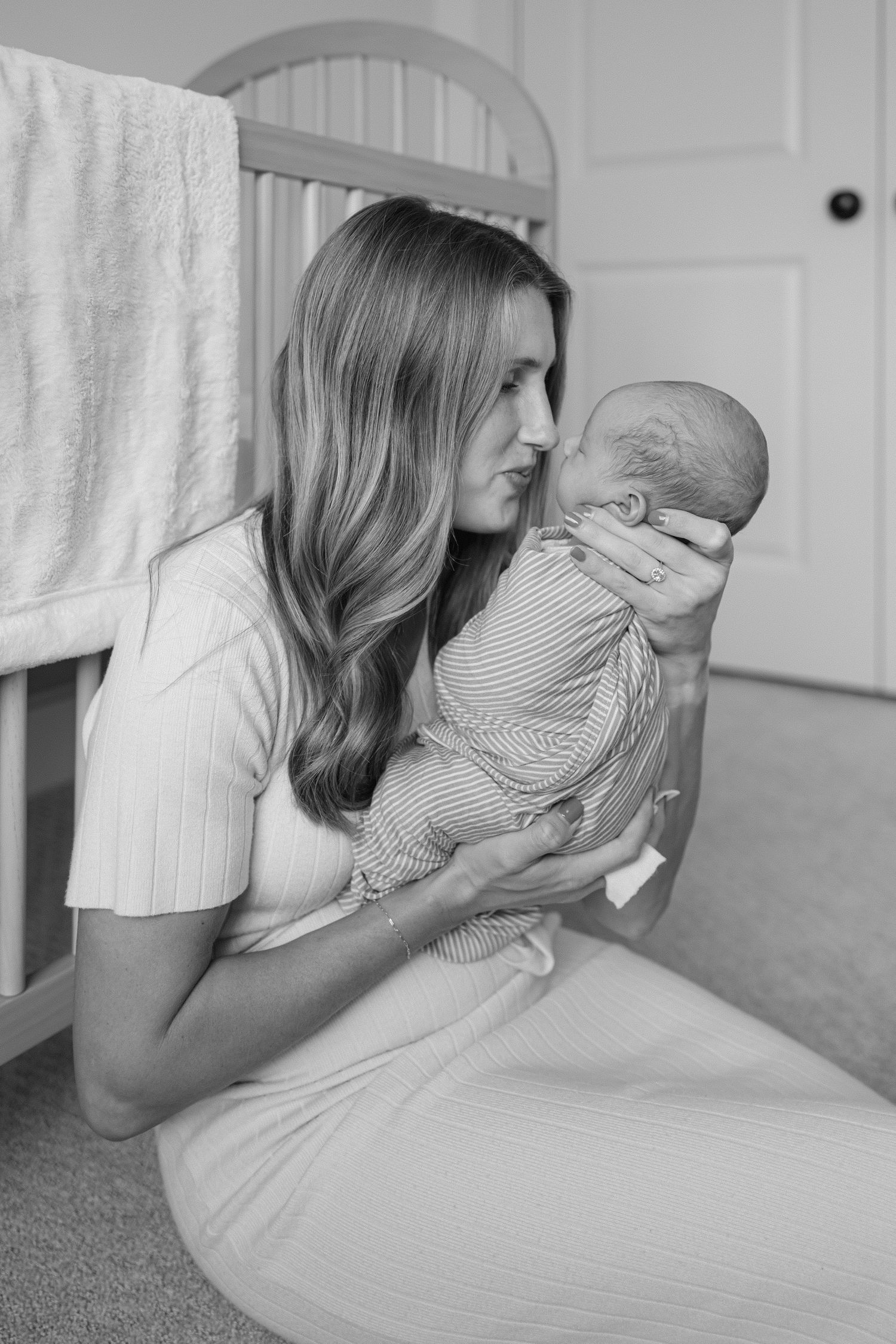 A tender moment between parent and newborn sitting on a nursery floor for their newborn photoshoot in Springville, Utah.