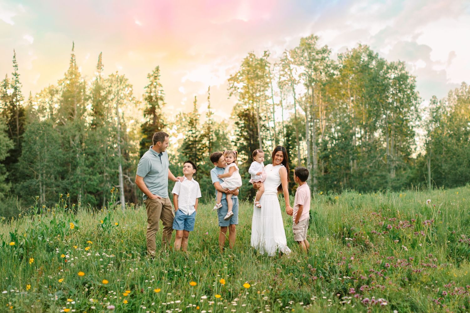 Family portrait in a wildflower meadow at golden hour with tall trees and a colorful sky backdrop in Heber, Utah.