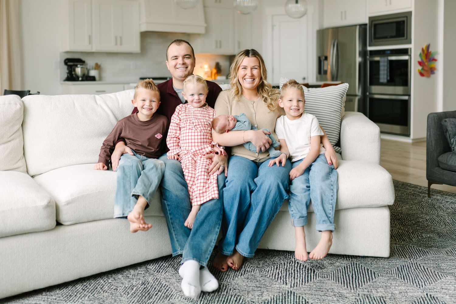Family lounging together on white couch in modern living room for their newborn photoshoot in Springville, Utah.