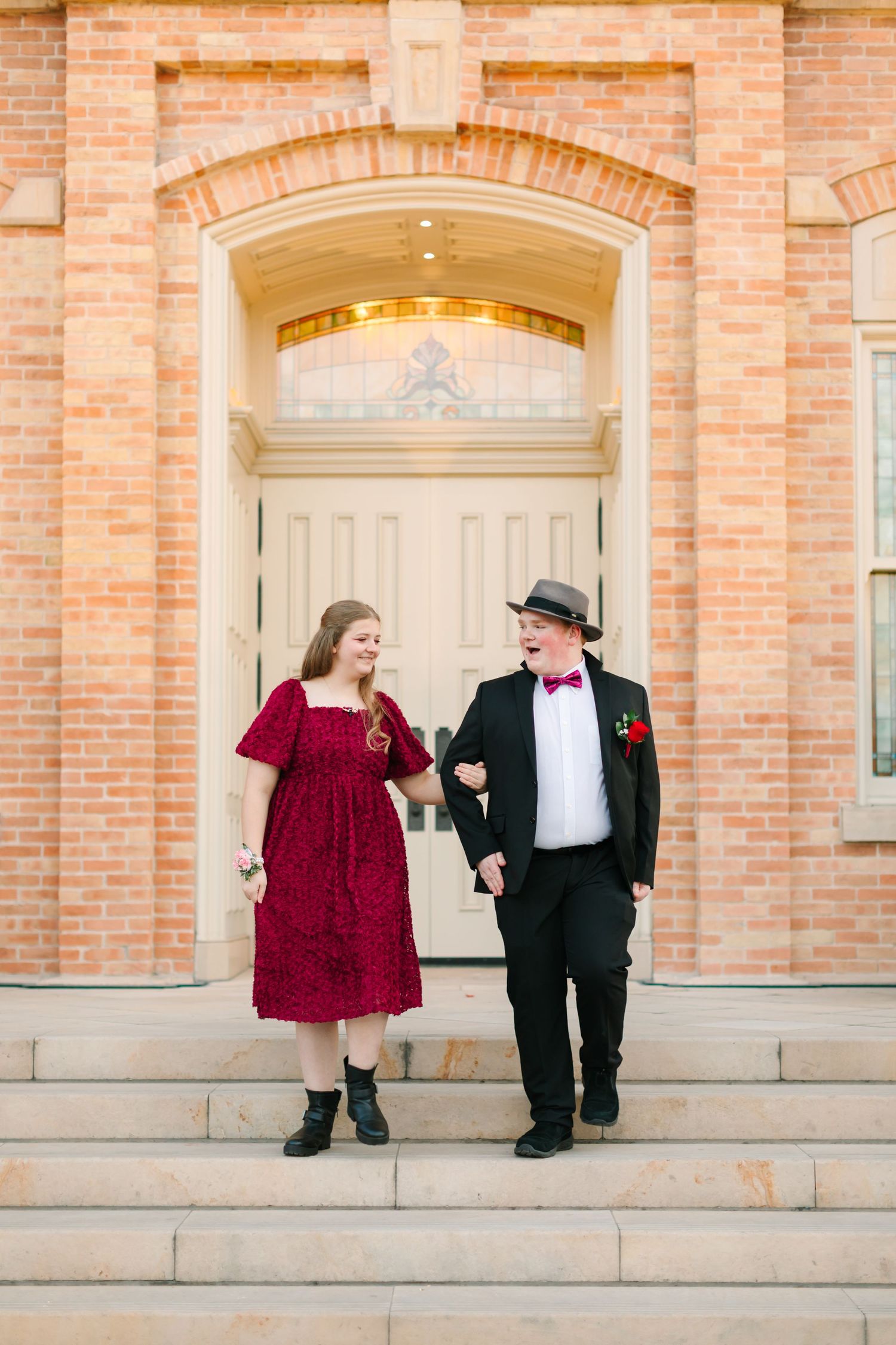 Couple in formal attire stands together against brick wall with arched doorways in elegant wedding photo series.