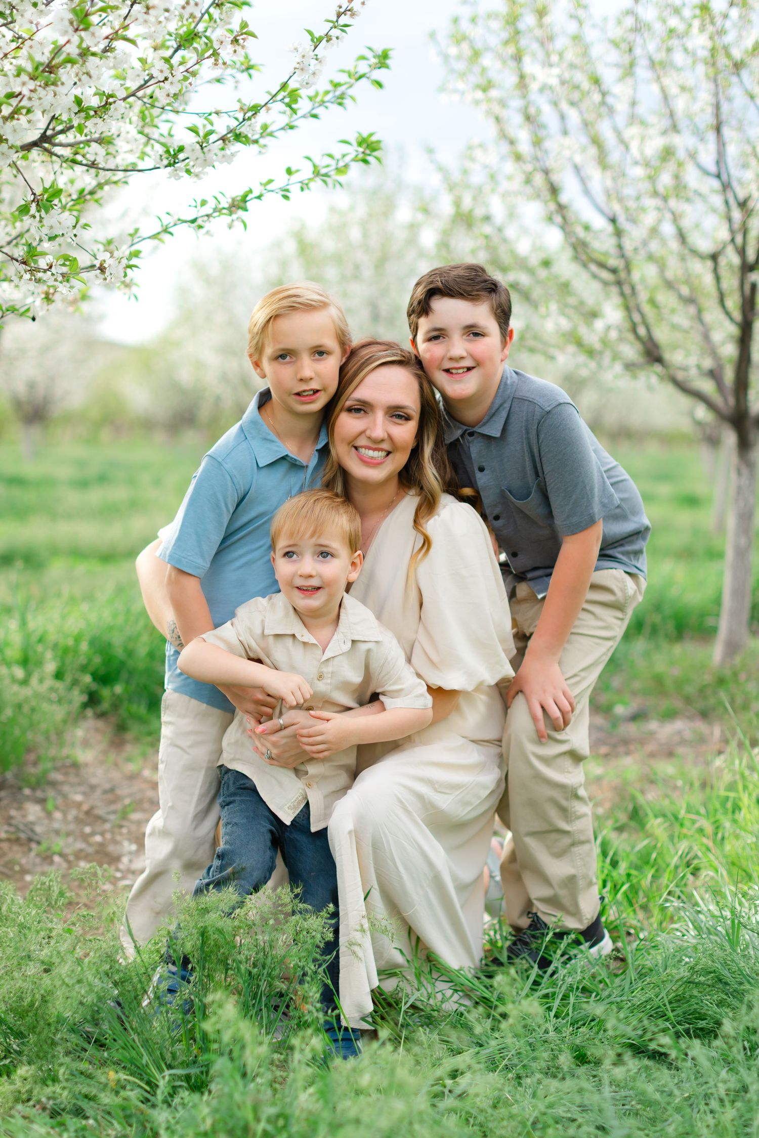 A family poses together in a blooming spring orchard with white blossoms and green grass.