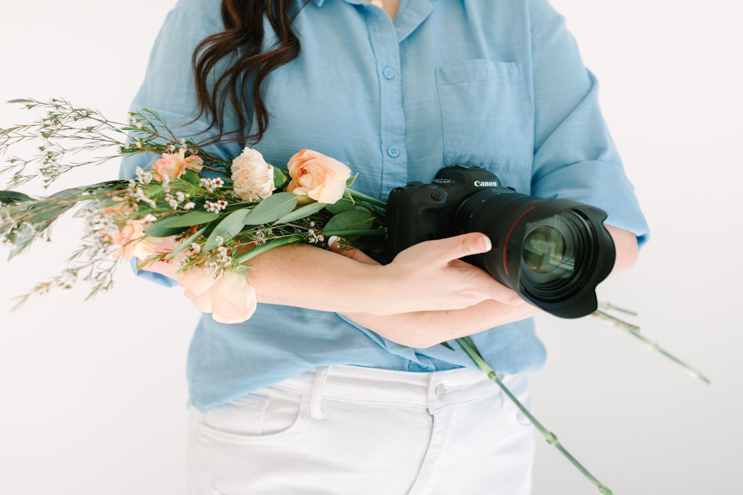 A person in a blue shirt lies down surrounded by delicate peach roses and white flowers in a dreamy composition.