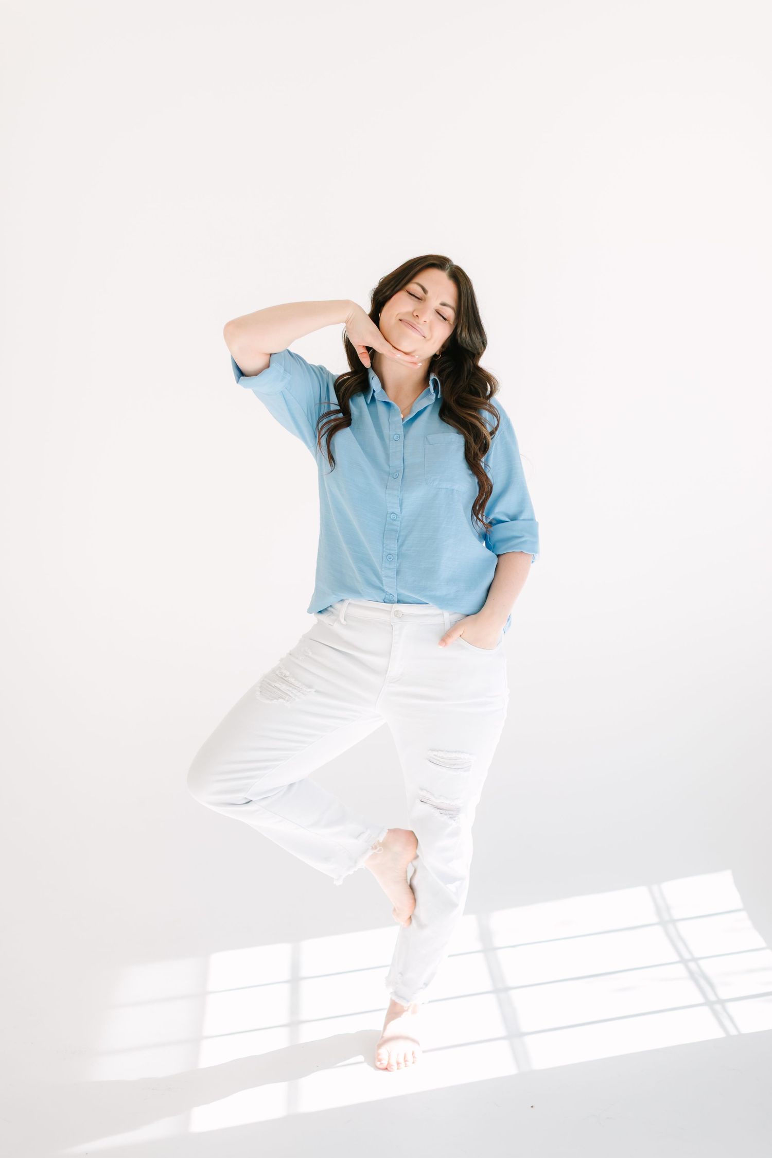 Photographer in blue shirt and white pants poses casually in bright studio setting.