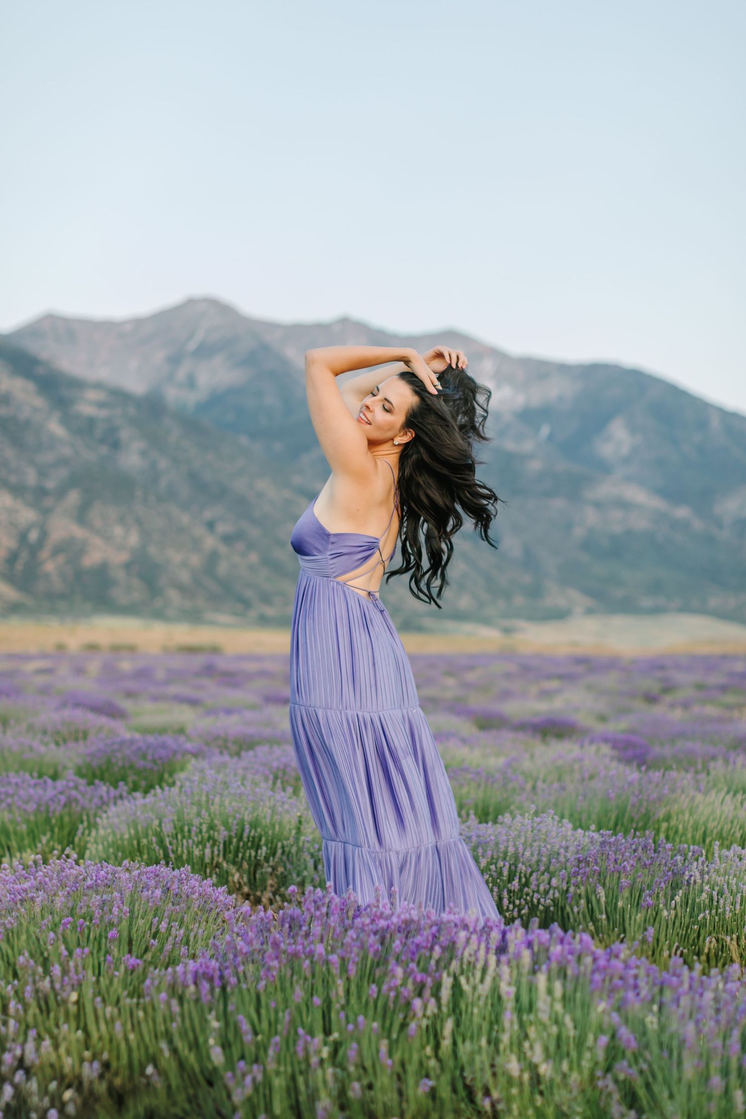 A flowing purple dress stands out against a mountain backdrop and blooming lavender field in soft evening light.