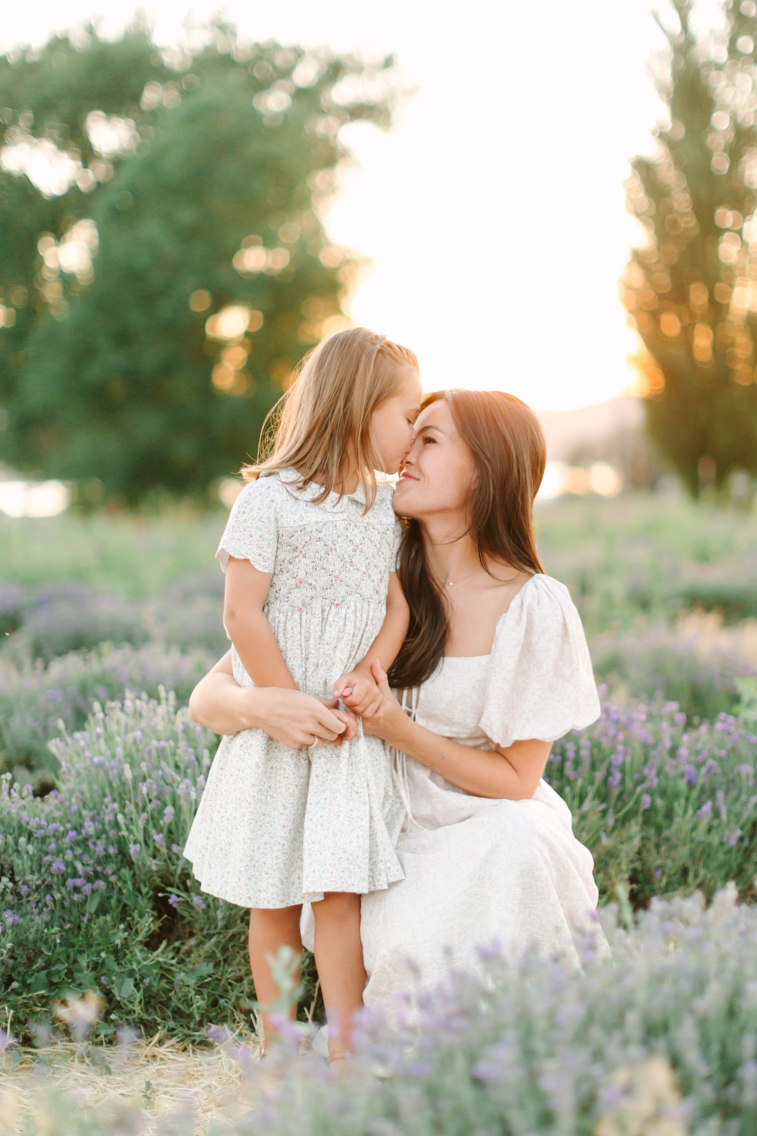 A tender moment shared between two people in white dresses among blooming lavender fields at sunset.