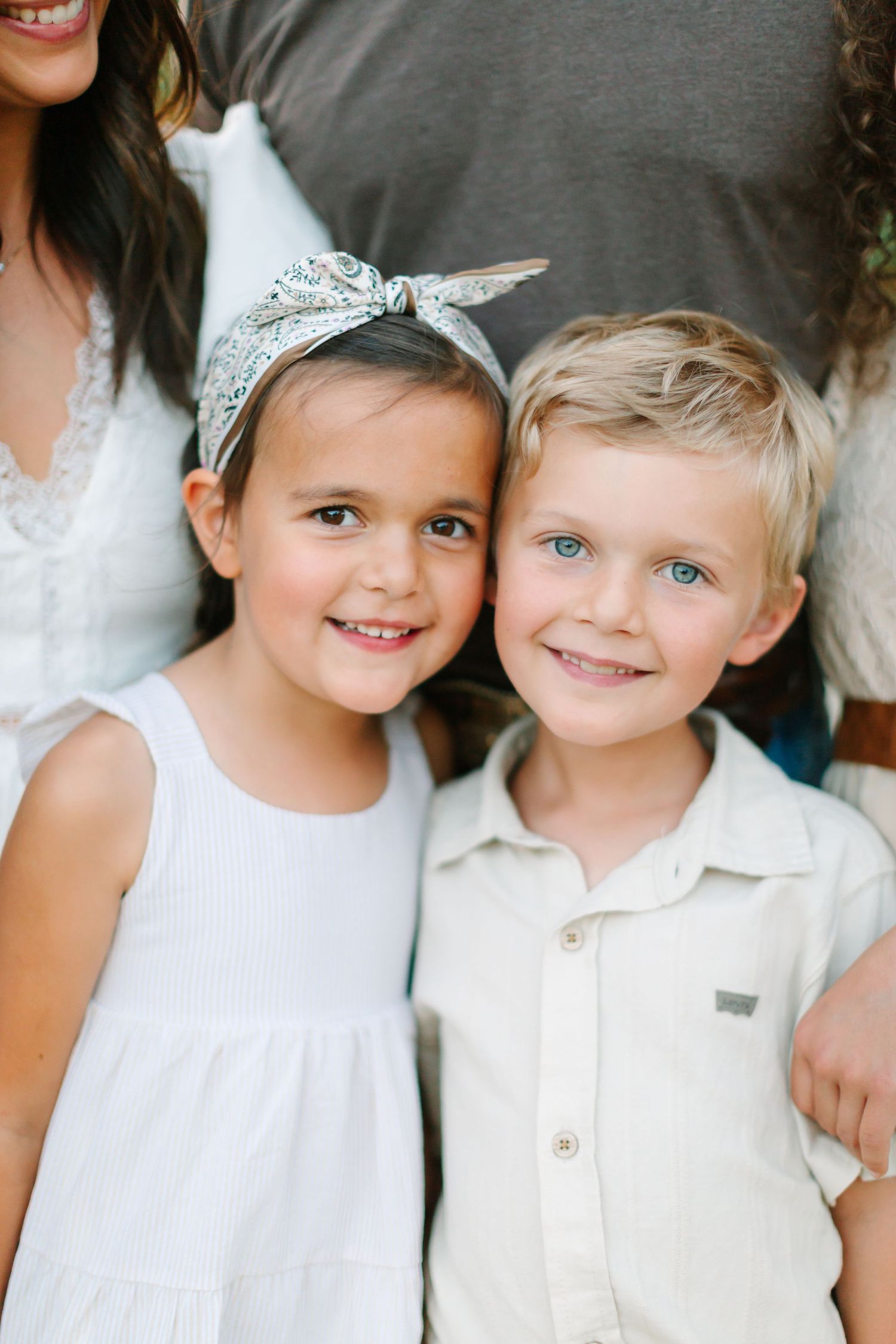 Two young children in white outfits smile together in a bright portrait photo.