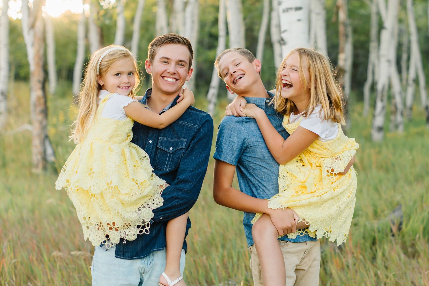 A group in casual attire poses together in a birch forest during golden hour sunlight.