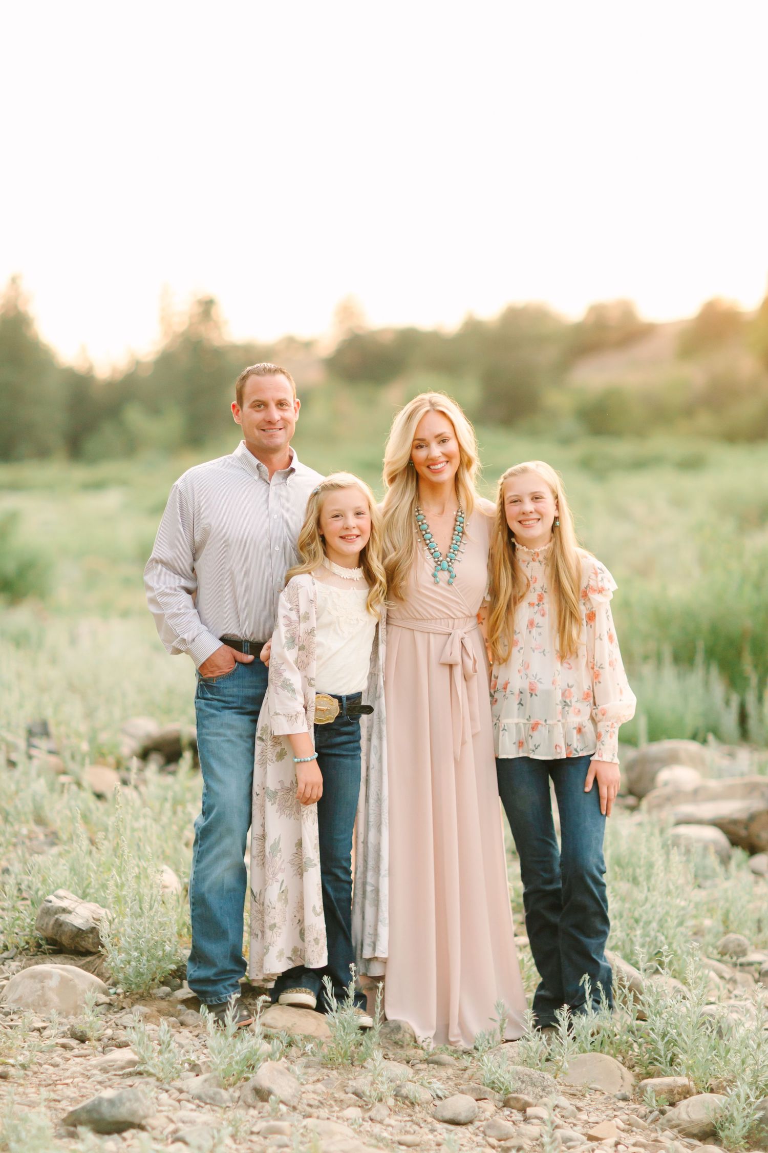 A family stands together in a field at sunset wearing coordinated neutral-toned outfits.