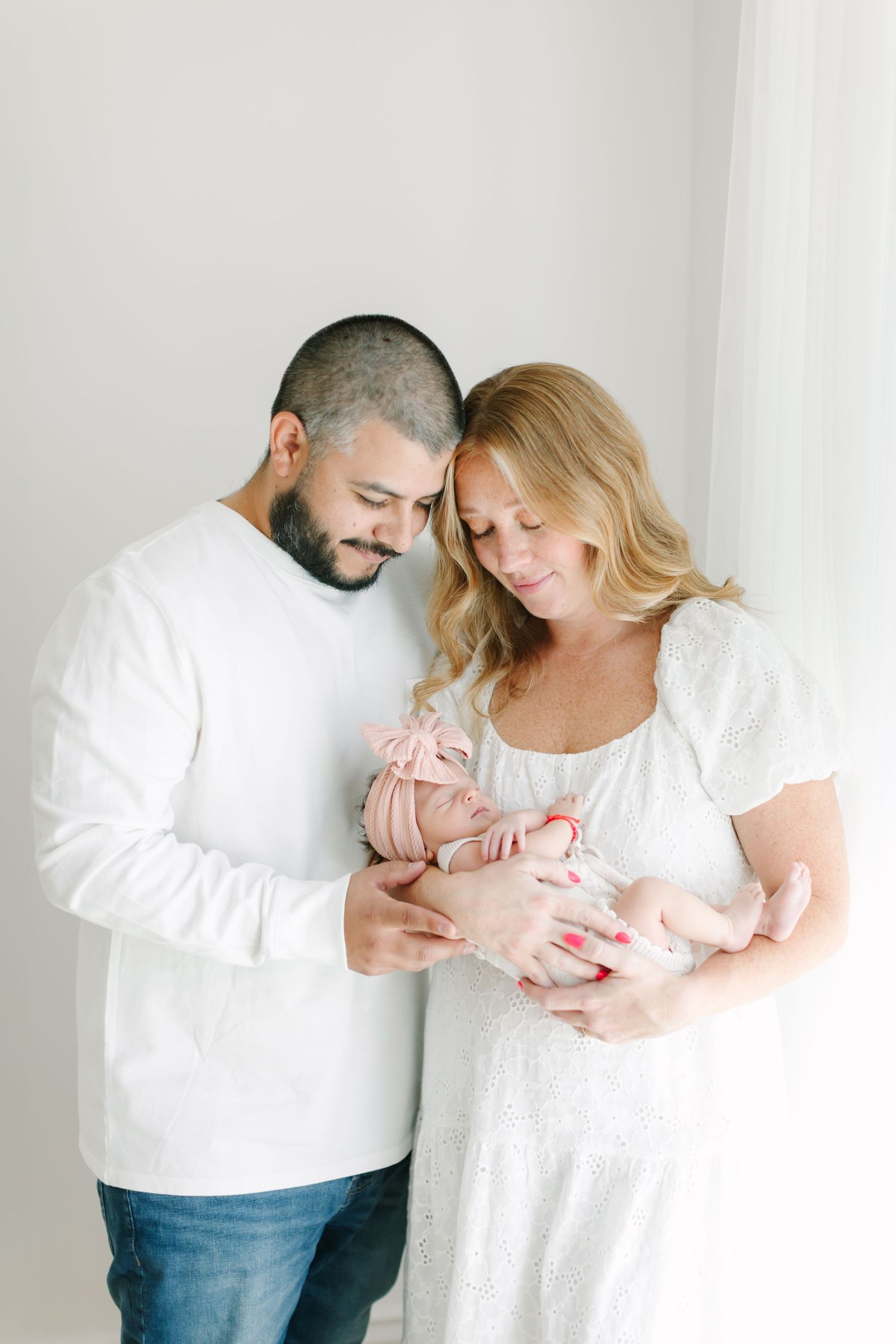 Parents in white shirts sharing tender moments with their newborn baby against white background.