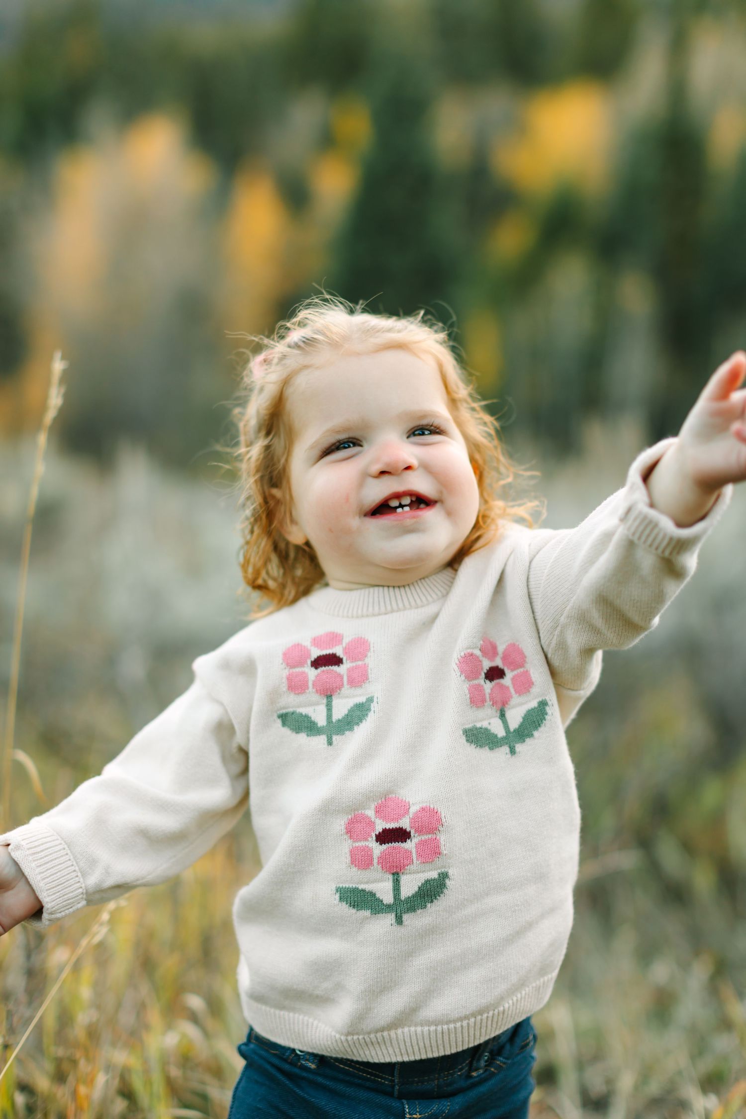 A child in a white floral sweater plays joyfully outdoors in a field on a sunny autumn day.