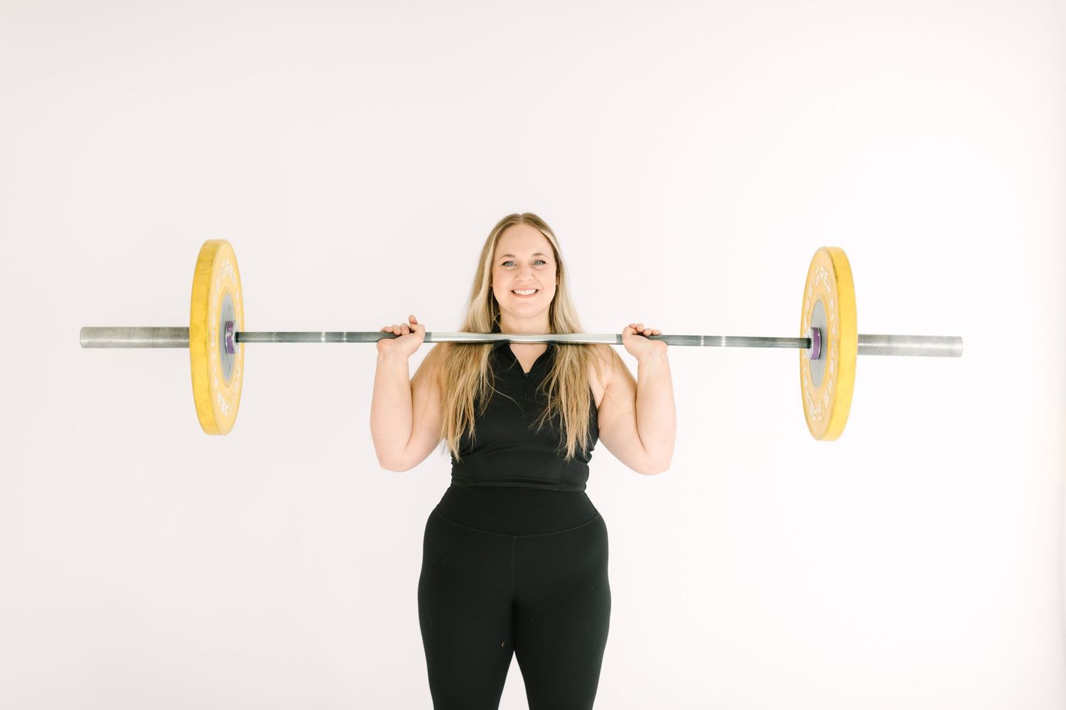 A person in black athletic wear performs a barbell overhead press sequence against a white background.