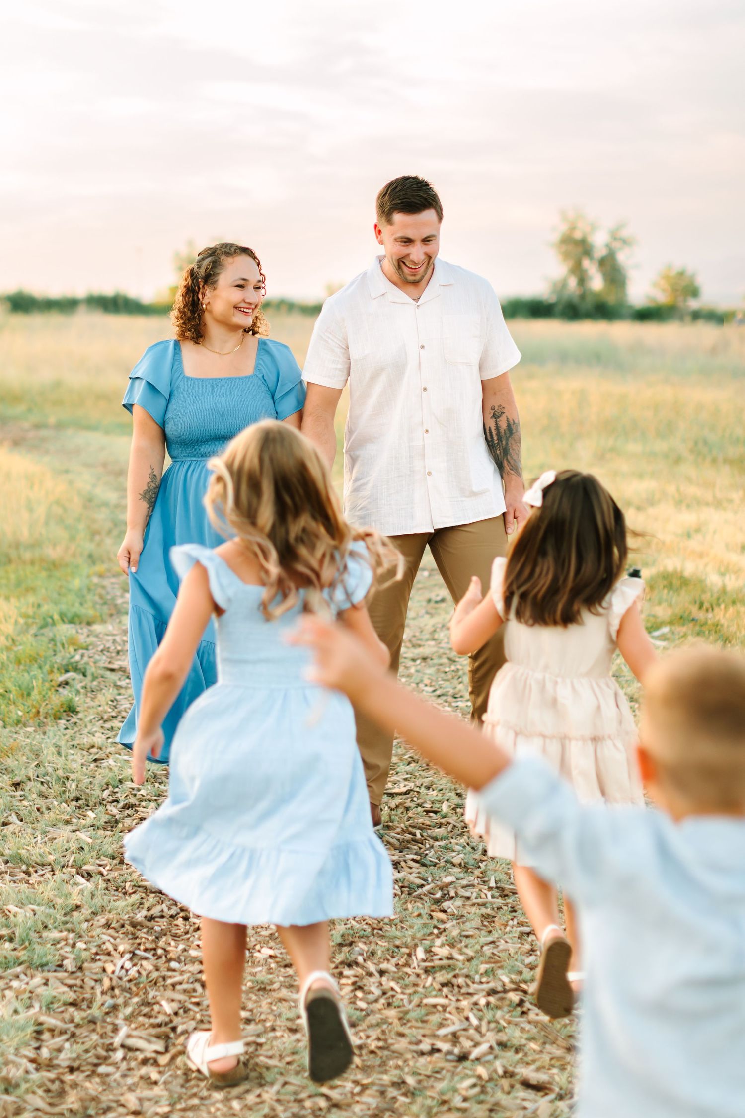Happy family with three young children running toward smiling parents in a sunny field at golden hour in Bountiful, Utah.